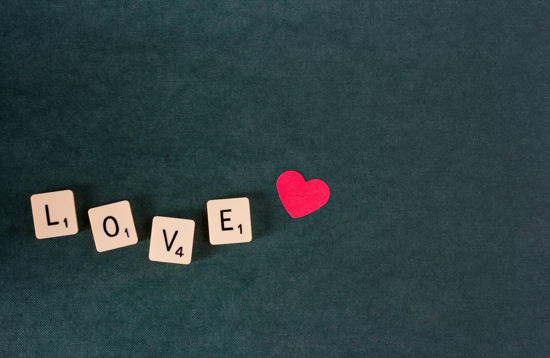 Scrabble tiles forming the word 'LOVE' with a red heart on a green background. - love languages explained
