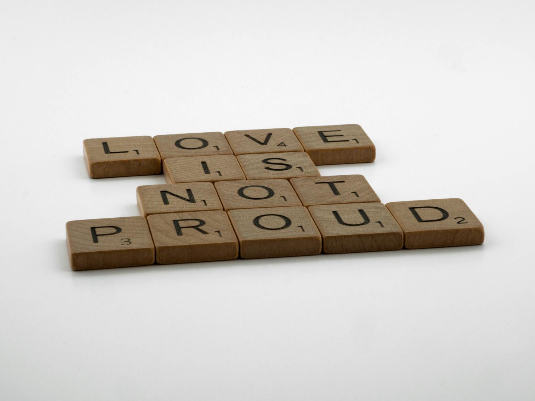 Creative arrangement of wooden letter tiles spelling 'Love is not proud' on a white background. - love languages explained
