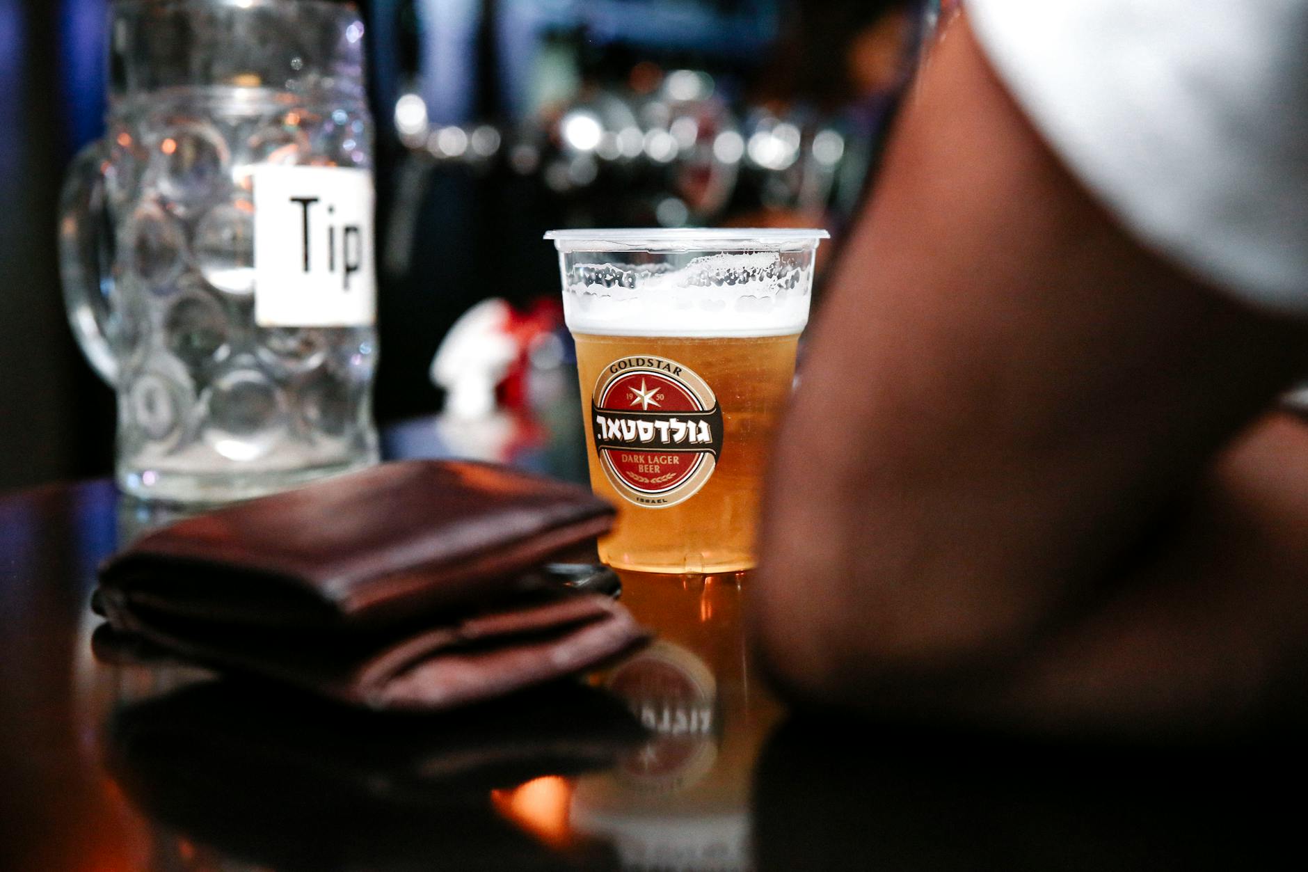 A close-up shot of a beer in a plastic cup on a bar counter, with a tip jar and wallet nearby. - marriage maintenance tips