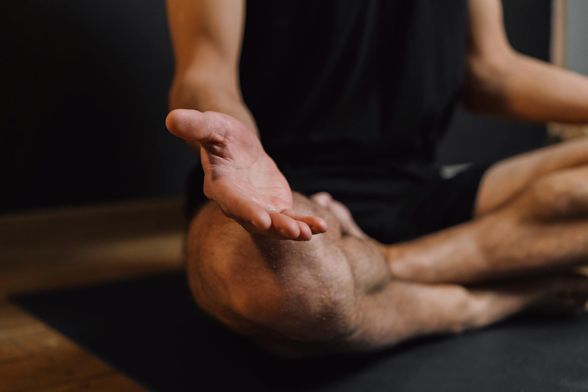 Crop unrecognizable barefoot male sitting with crossed legs on sports mat during stress relief meditation session - mental clarity techniques