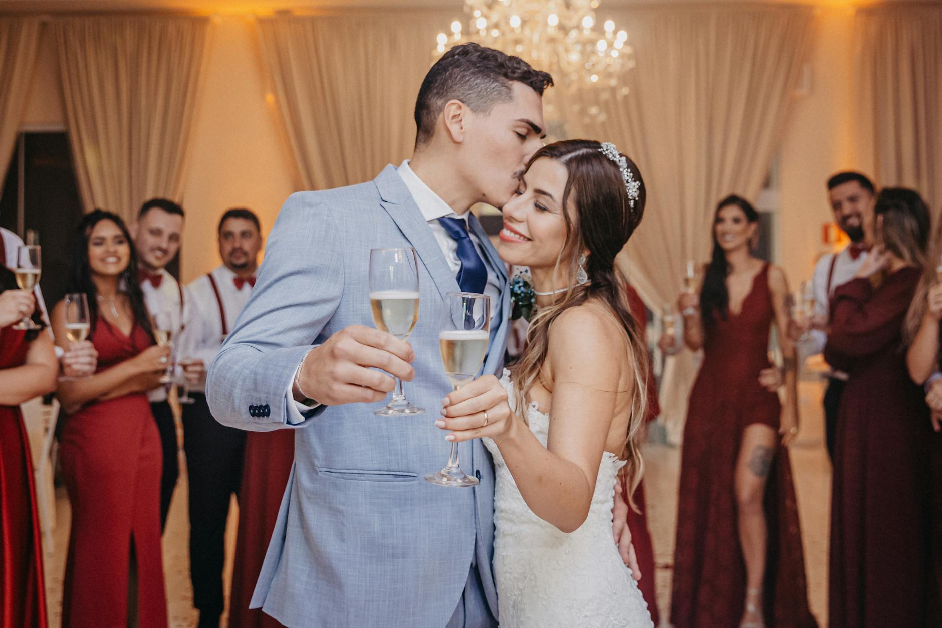 Newlywed couple enjoying a romantic kiss and champagne toast at their wedding celebration, surrounded by guests. - newlywed marriage advice