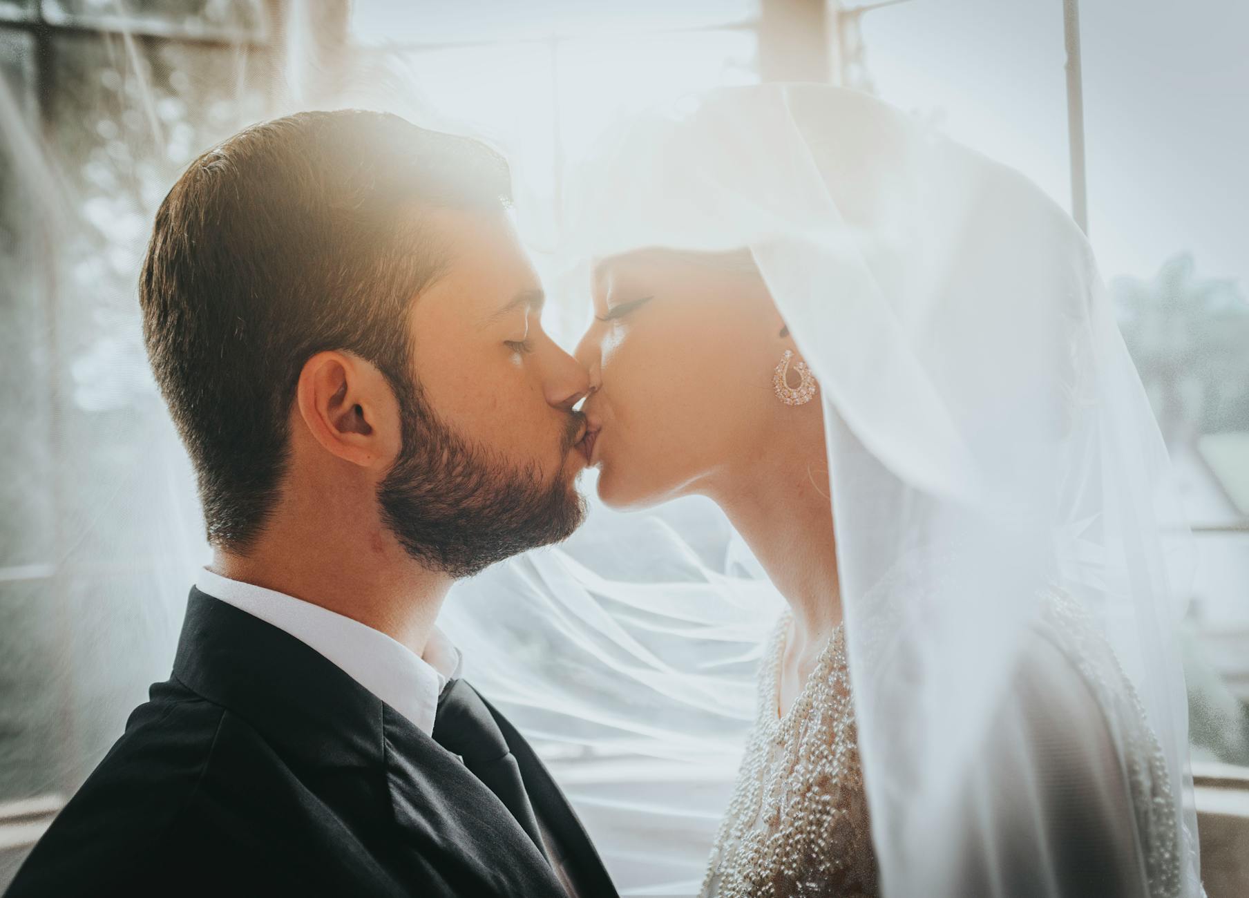 A bride and groom share a romantic kiss in elegant wedding attire, indoors with soft lighting. - newlywed marriage advice