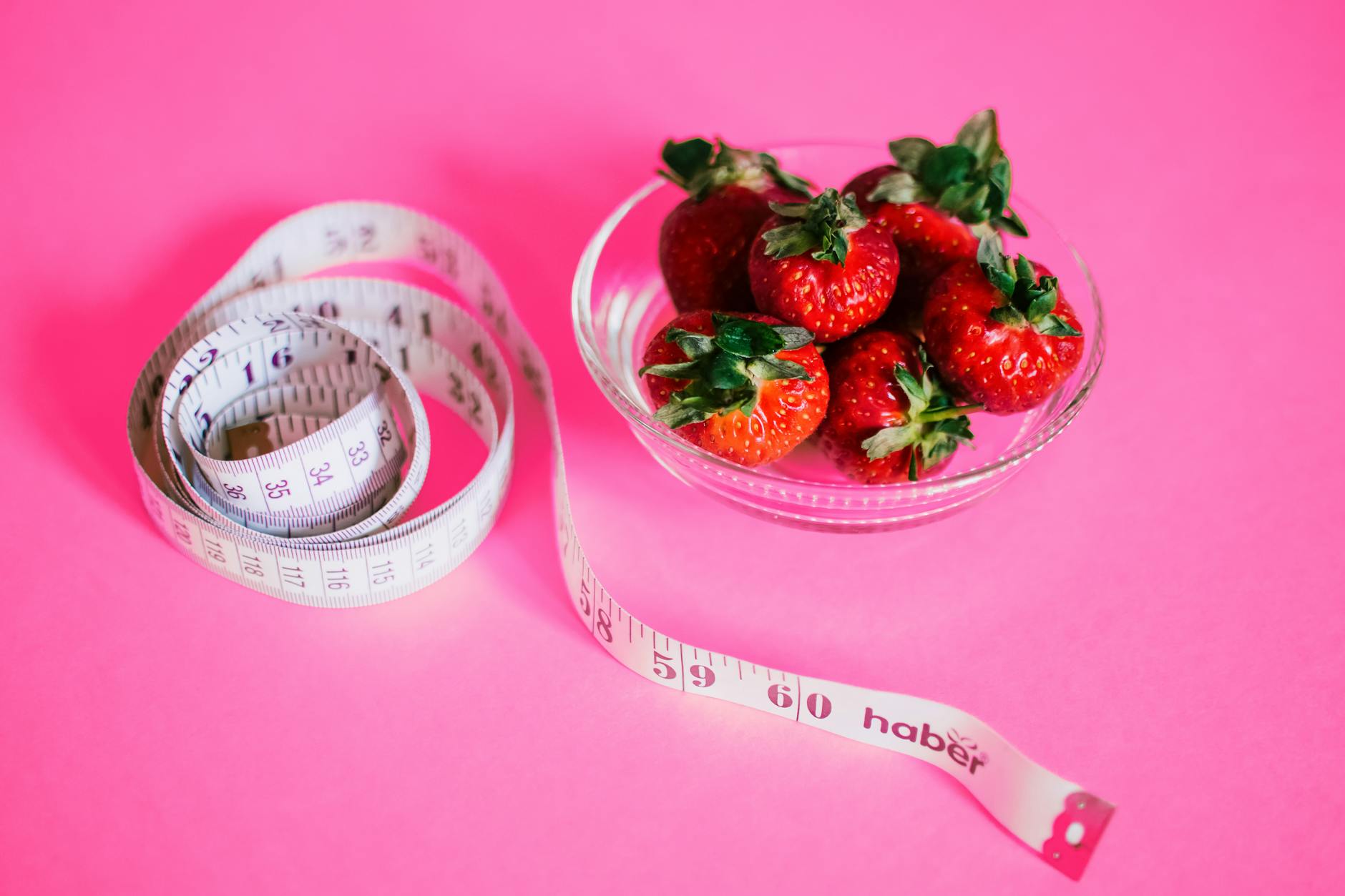 A glass bowl of fresh strawberries paired with a pink measuring tape symbolizes healthy eating. - outdoor play benefits