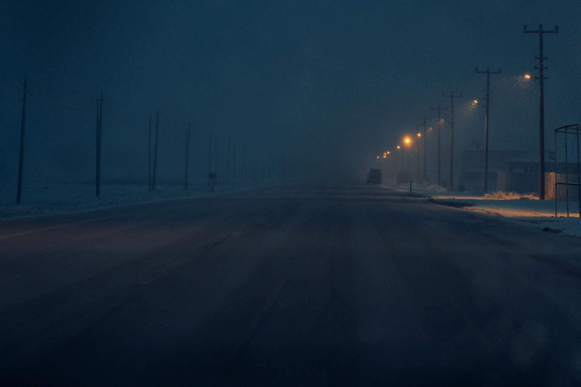A dark winter night on a snow-covered road lit by street lamps, creating a moody atmosphere. - overcome loneliness winter