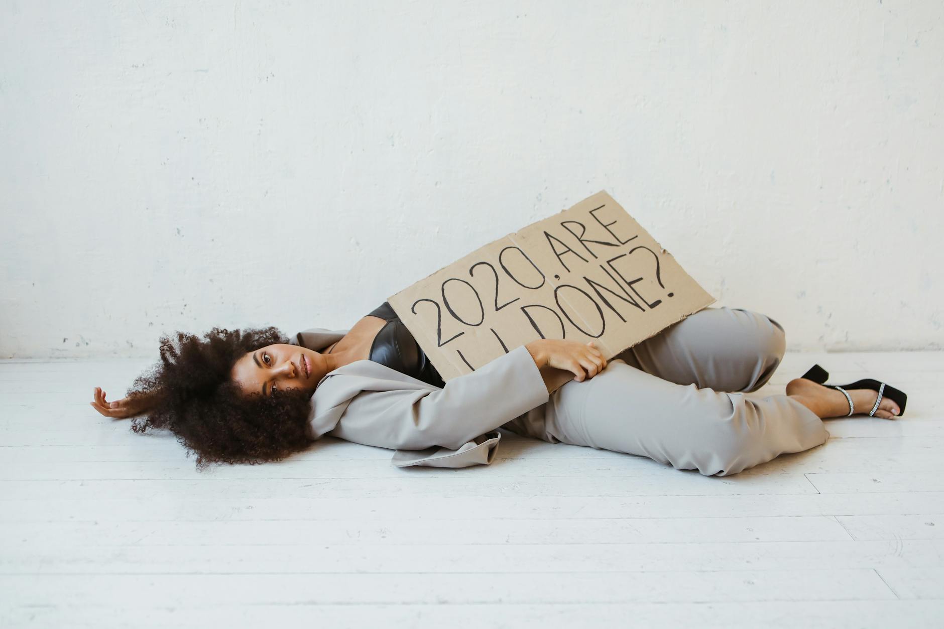 Exhausted woman holding a sign expressing 2020 burnout, lying indoors on a wooden floor. - overcome procrastination