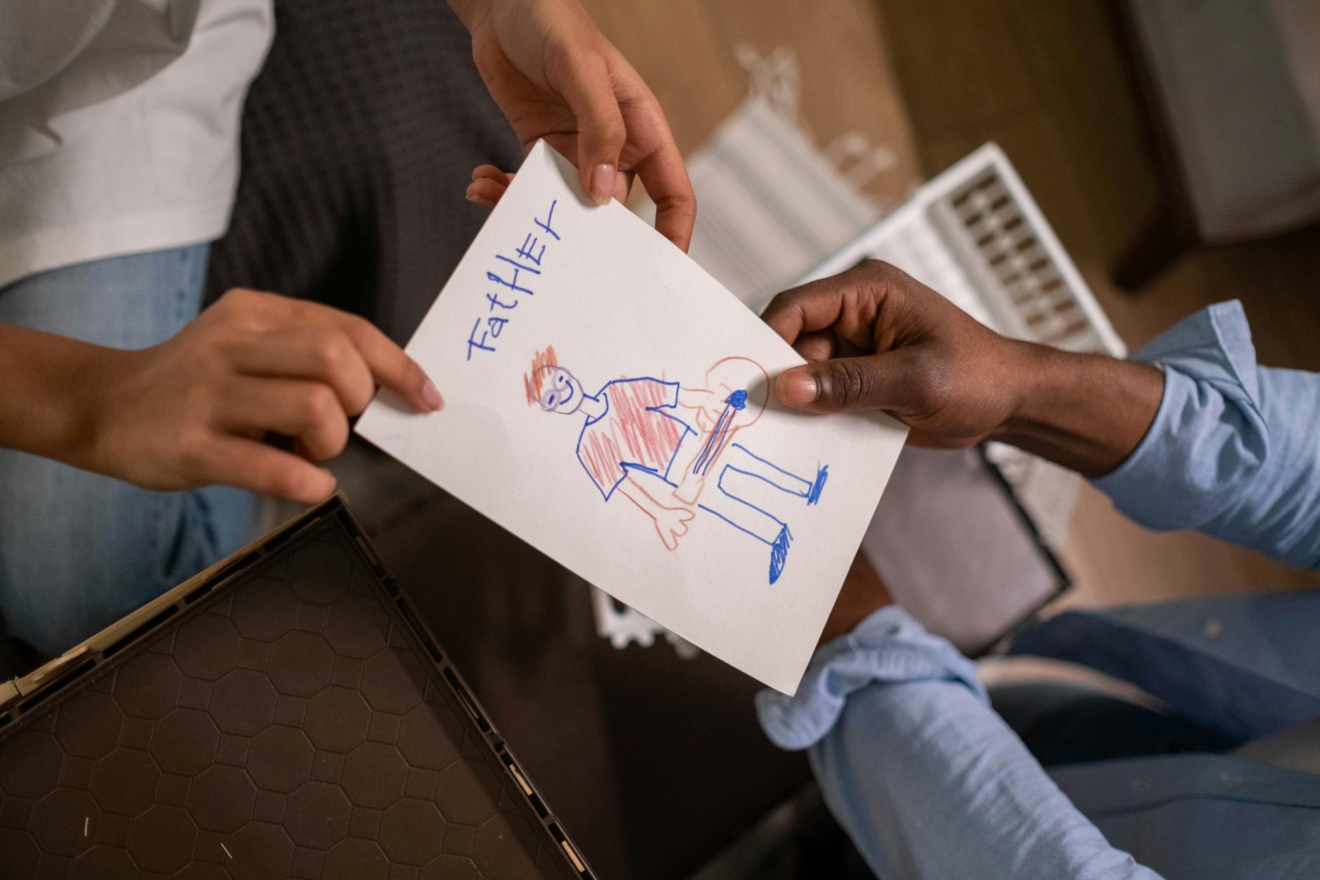A child hands a drawing labeled 'Father' to an adult indoors, showcasing family bonding and creativity. - parent child communication