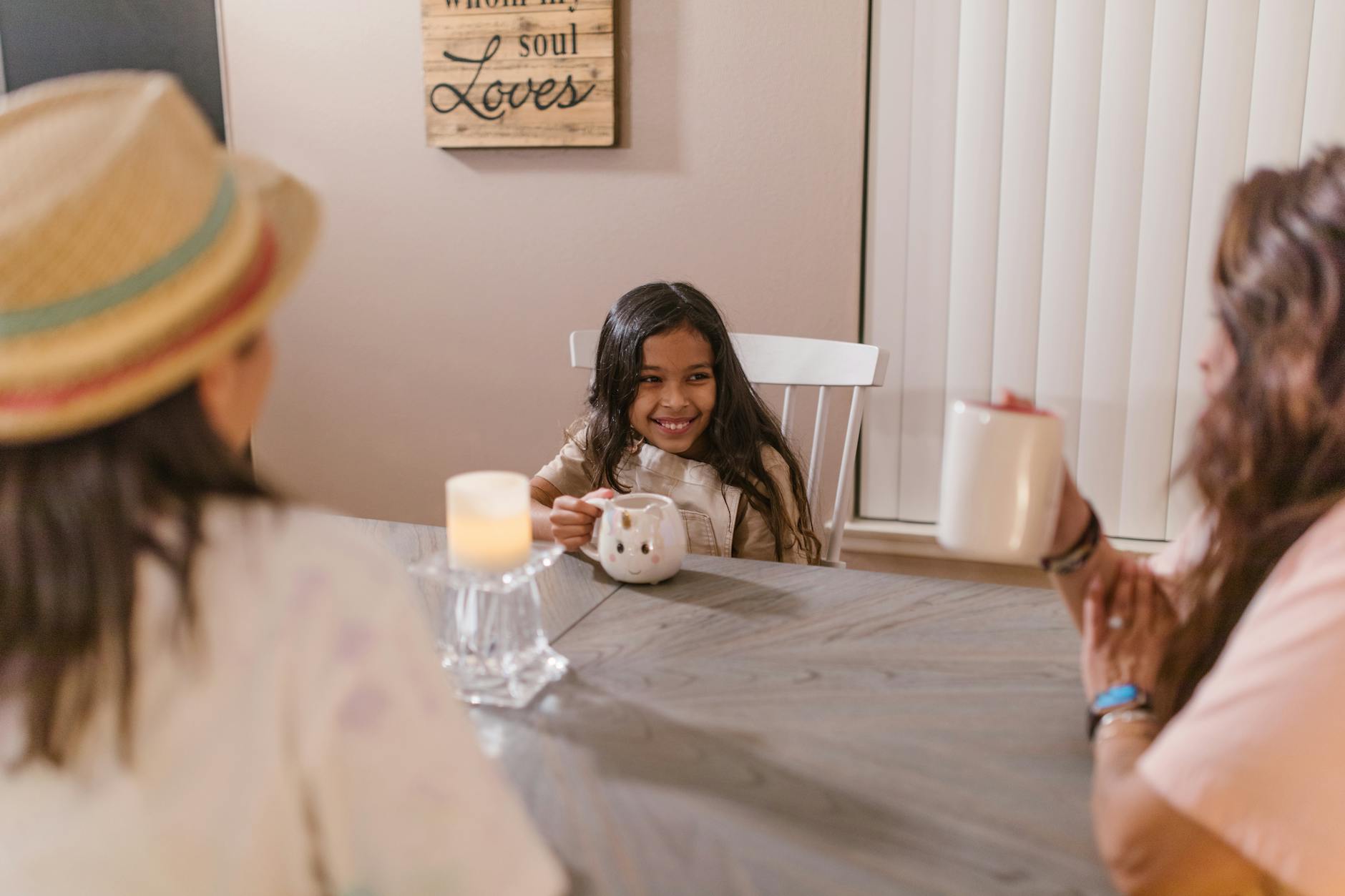 A joyful family moment with a smiling child engaging in conversation over ceramic mugs indoors. - parent child communication