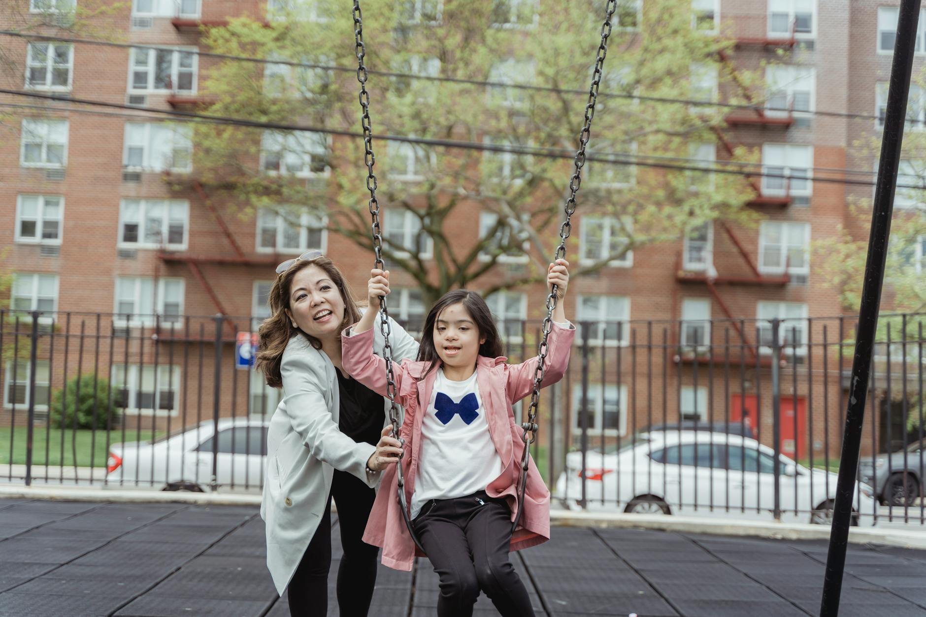 Mother and daughter having fun on a swing set in a city playground. - parent child communication