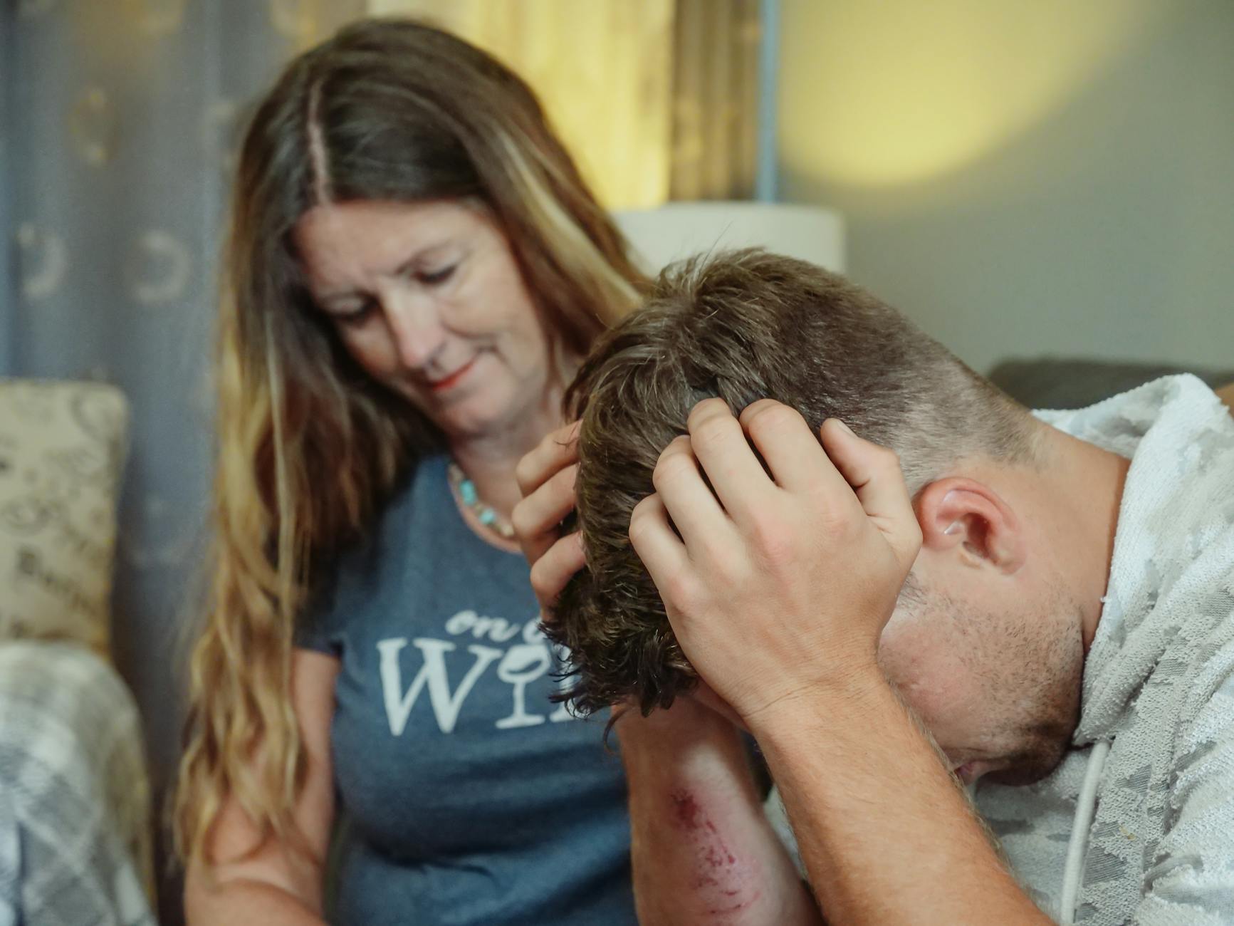 A mother provides emotional support to her stressed son indoors, conveying empathy and caring. - parental emotional support