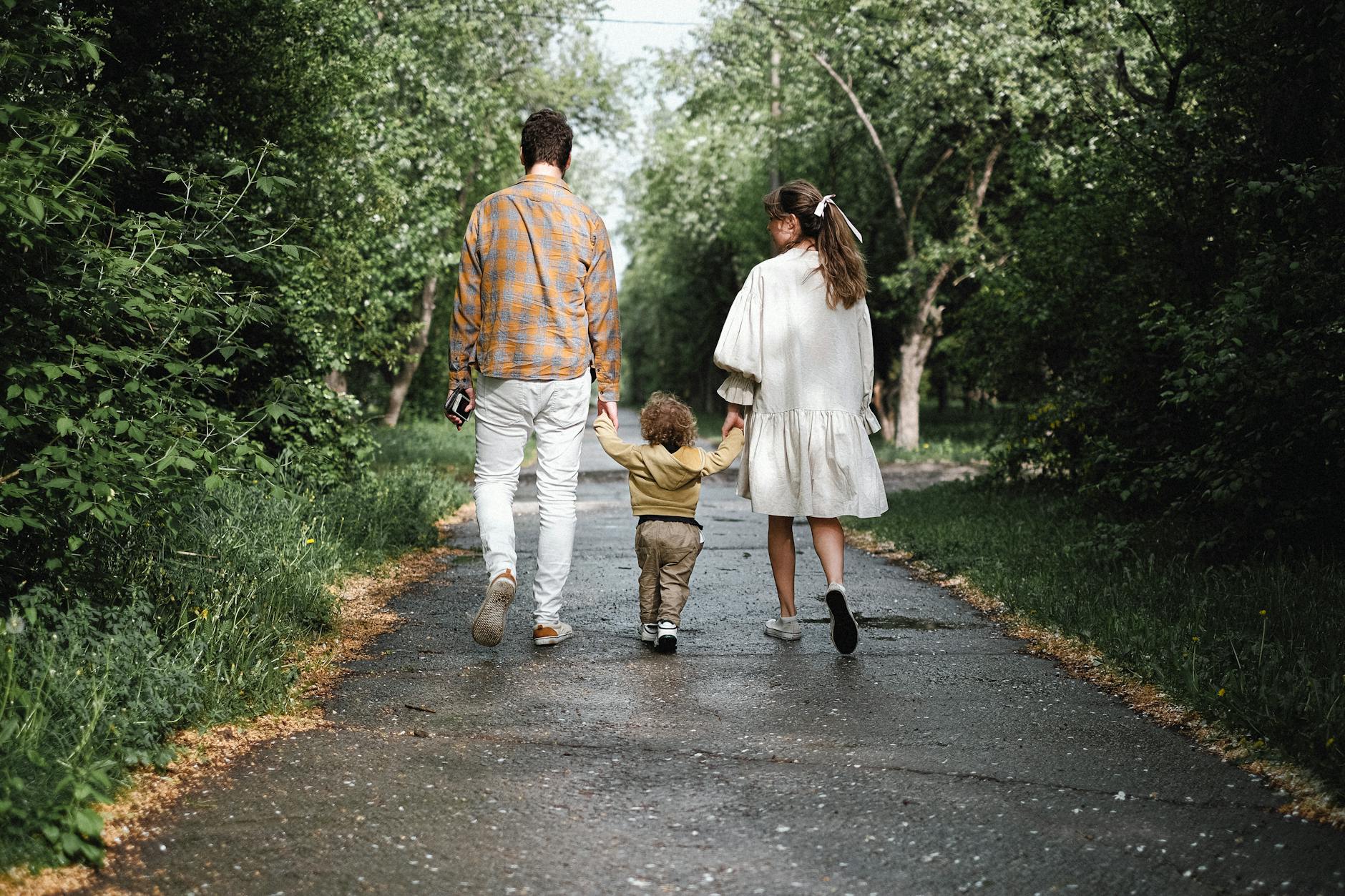A couple and toddler enjoy a peaceful walk on a tree-lined path in a lush park. - post divorce co parenting