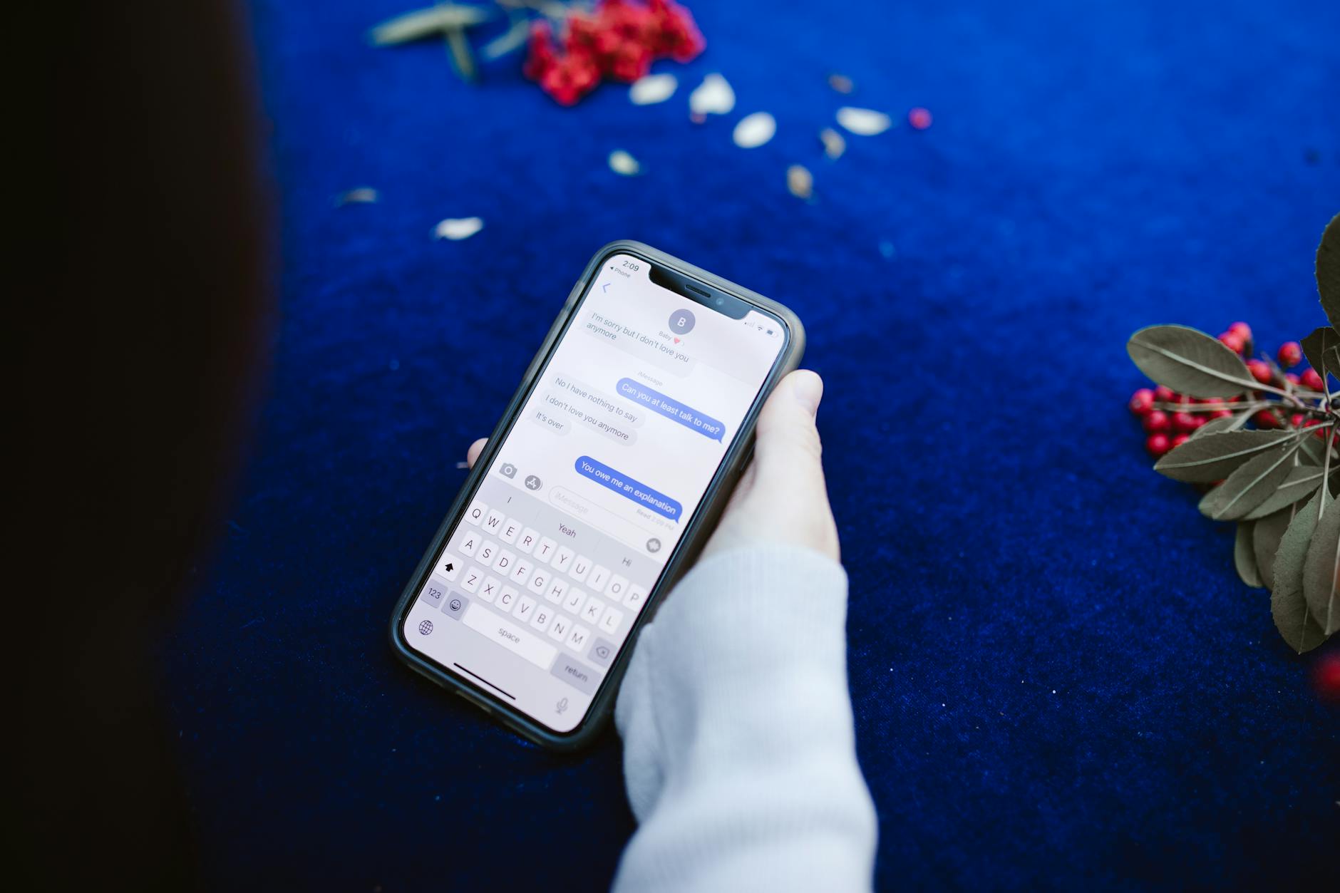 A person holding a smartphone displaying text messages on a blue surface with flowers. - post-hibernation conversations