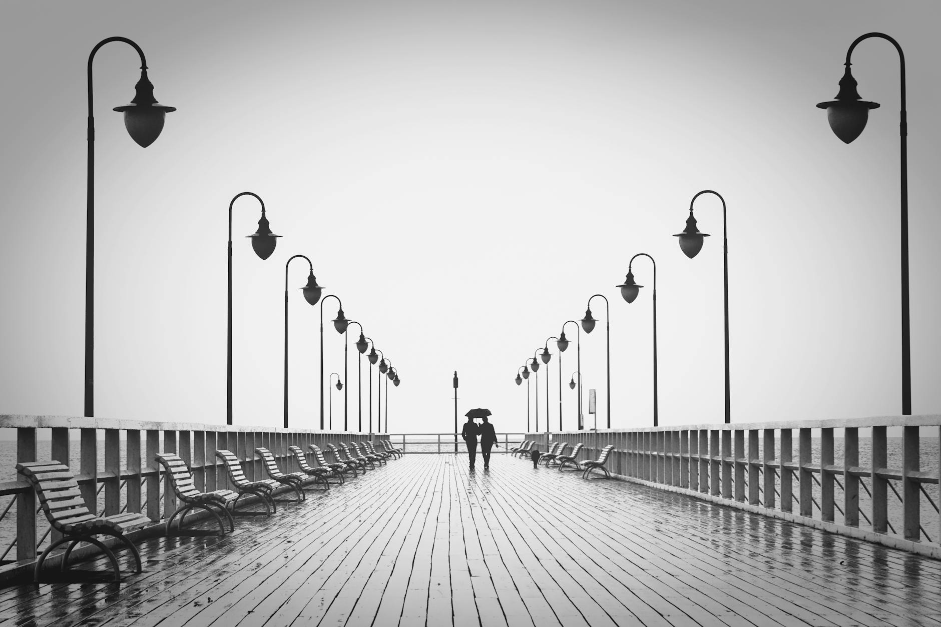 A couple holding umbrellas walks on a rainy boardwalk, embodying romance and tranquility. - post holiday relationship challenges
