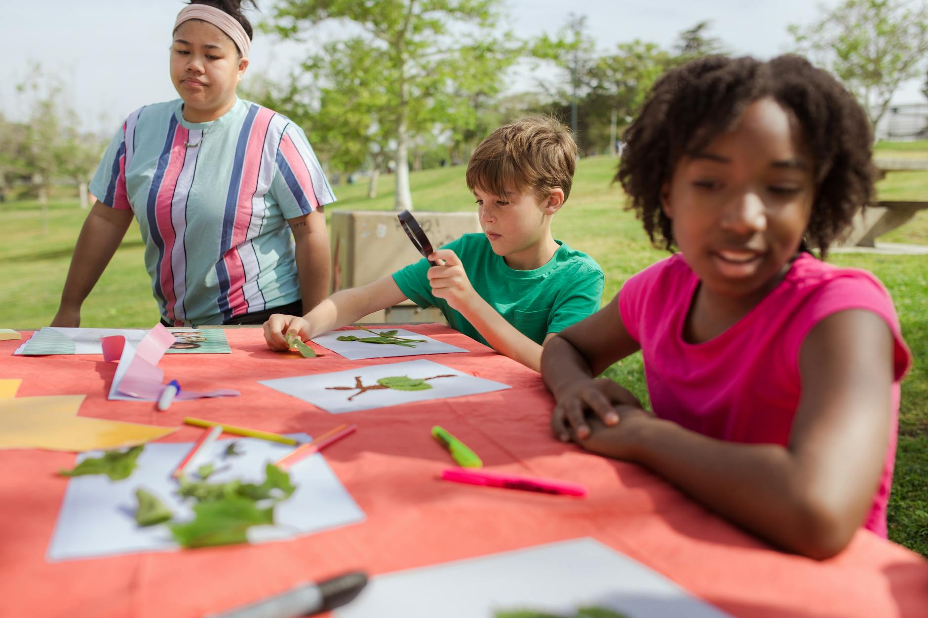 Kids engage in nature crafts outdoors, inspecting leaves with a magnifying glass, on a sunny day. - preschool nature activities