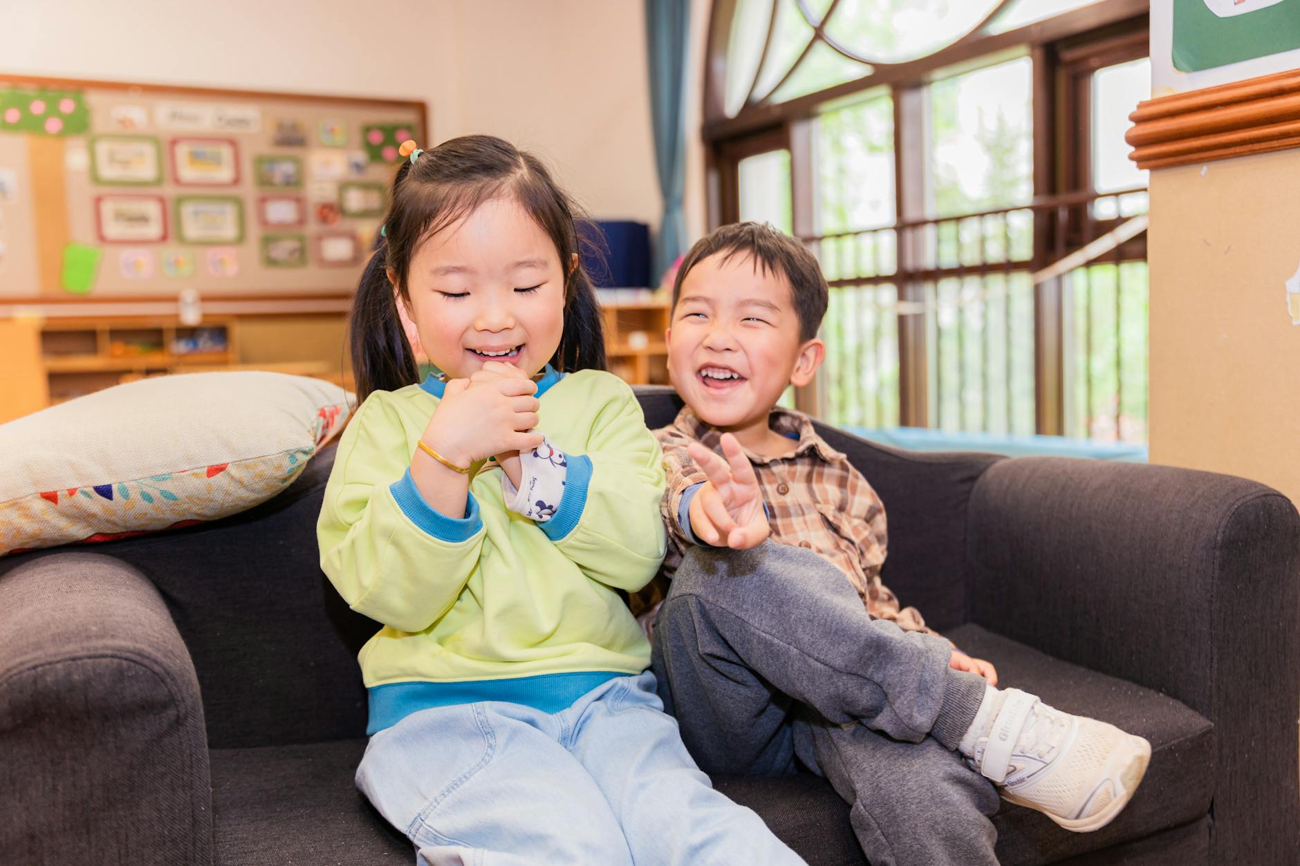 Two joyful children laughing and playing on a sofa in a classroom setting. - preschool outdoor learning