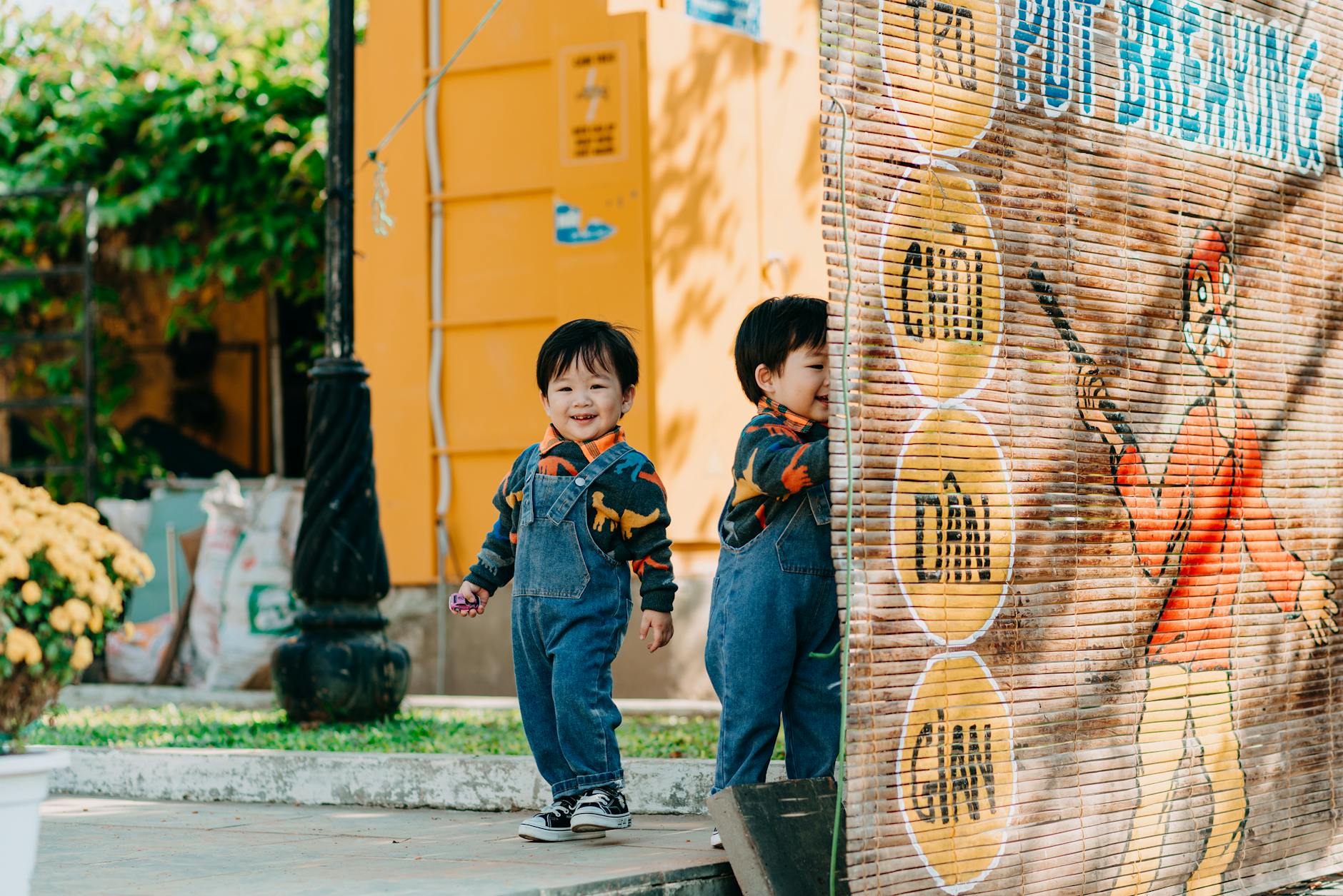 Smiling twin toddlers in denim jumpers playing outdoors, capturing the joy of childhood on a sunny day. - preschool playdate etiquette