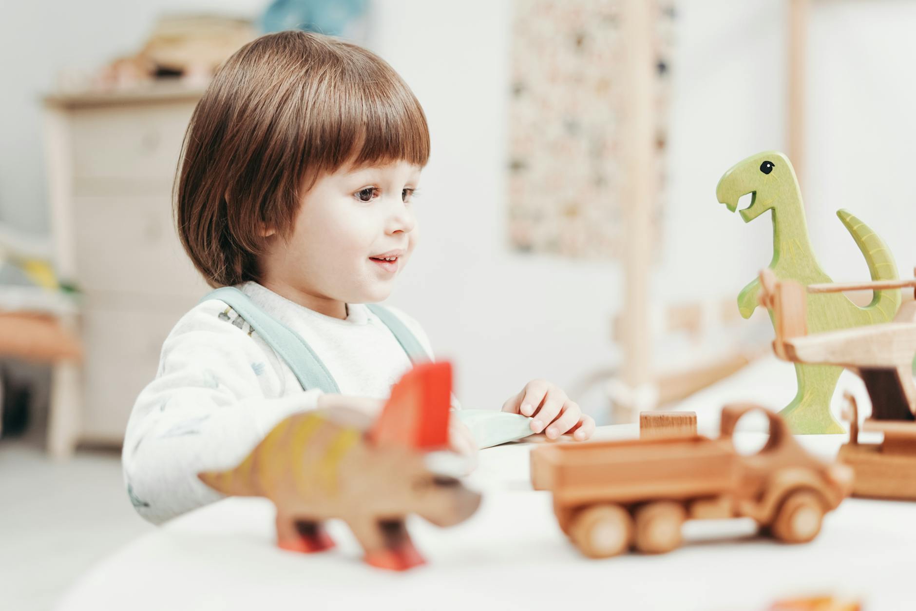 A happy child playing with wooden dinosaur toys in a bright playroom setting. - preschool playdate etiquette