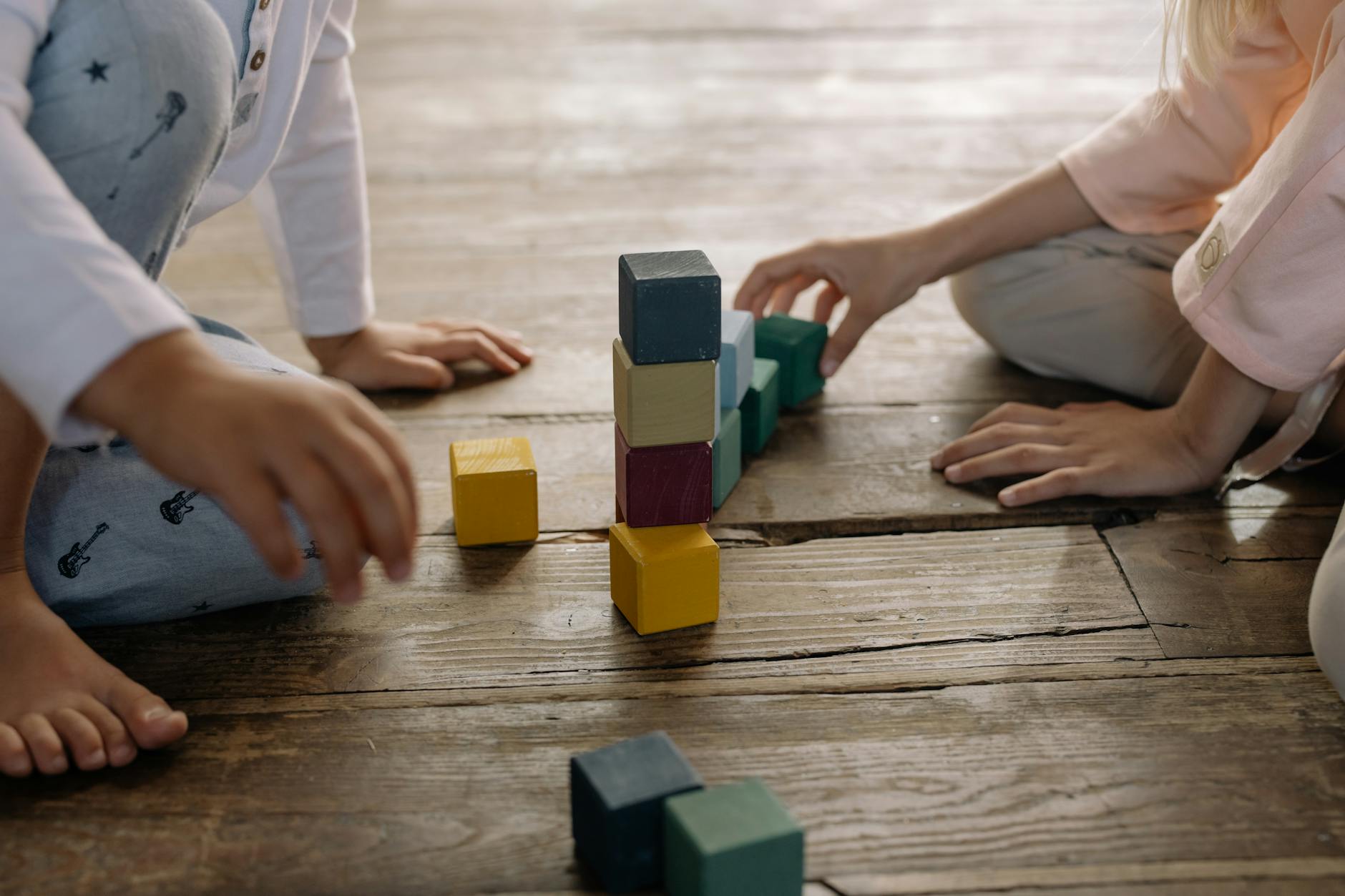 Kids engaged in building with multicolored wooden blocks on a wooden floor. - preschool social skills