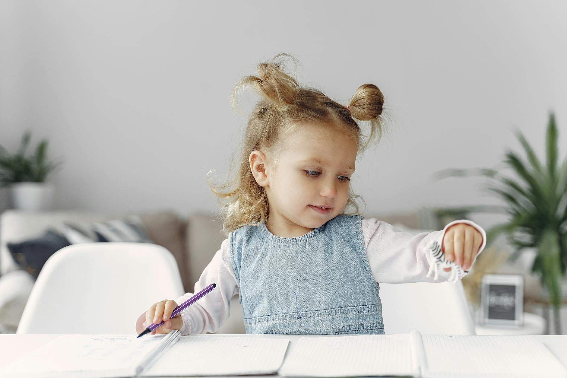 Young girl engaged in playful and creative learning with a toy and notebook indoors. - preschooler independence