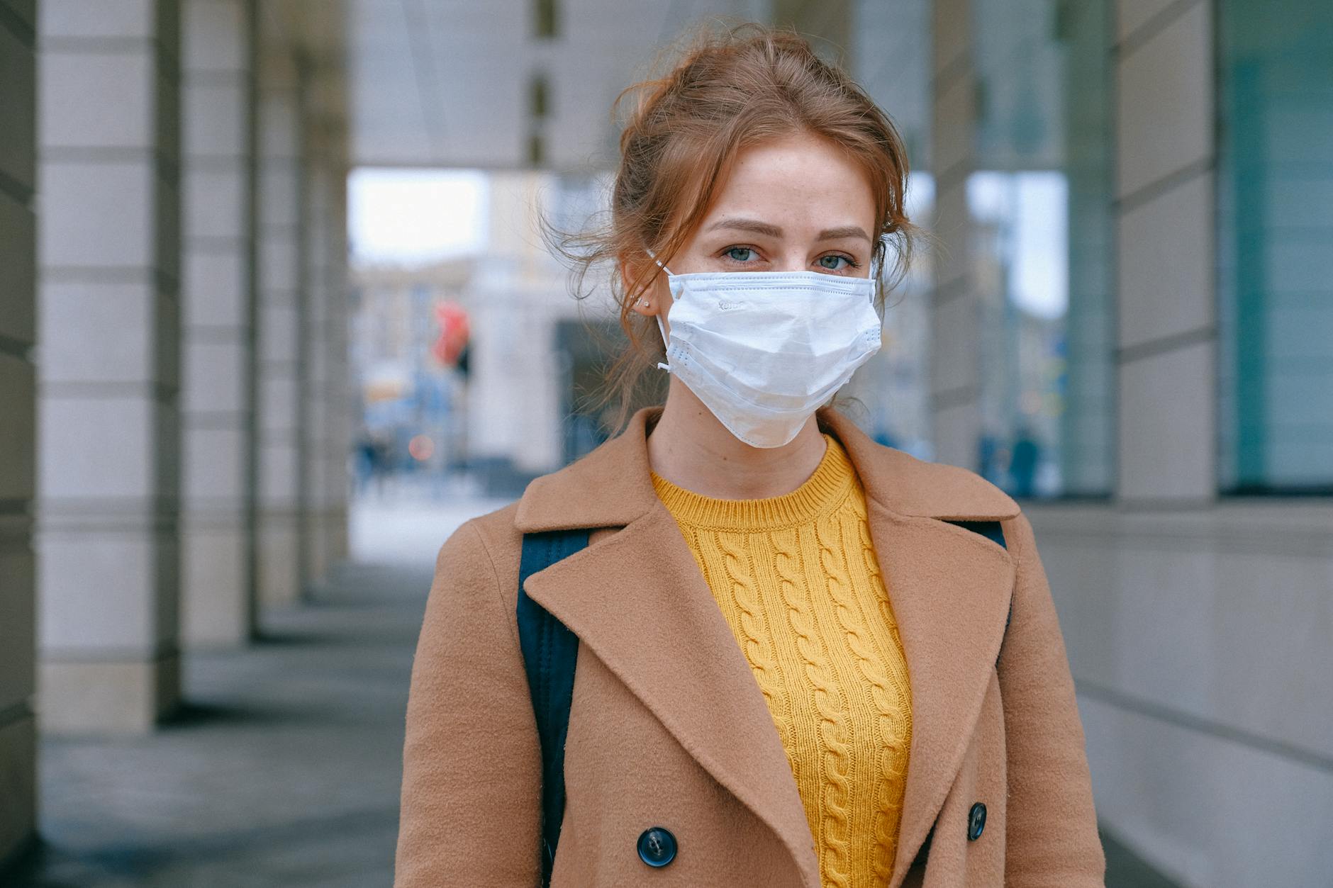Young woman in a coat and mask stands outdoors, promoting health and safety measures. - prevent spring s.a.d.