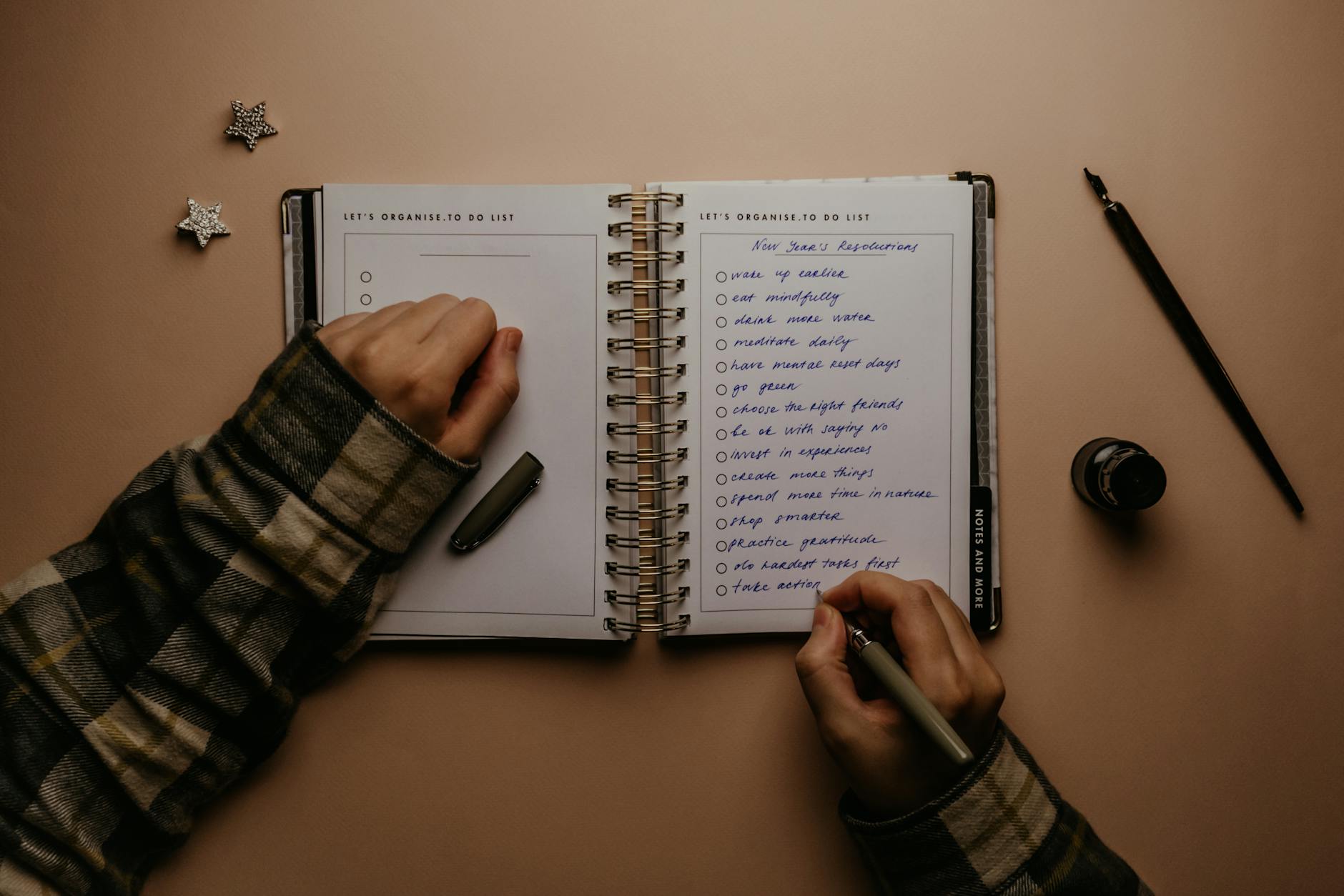Overhead shot of a person writing New Year's resolutions in a notebook on a desk. - realistic personal growth goals