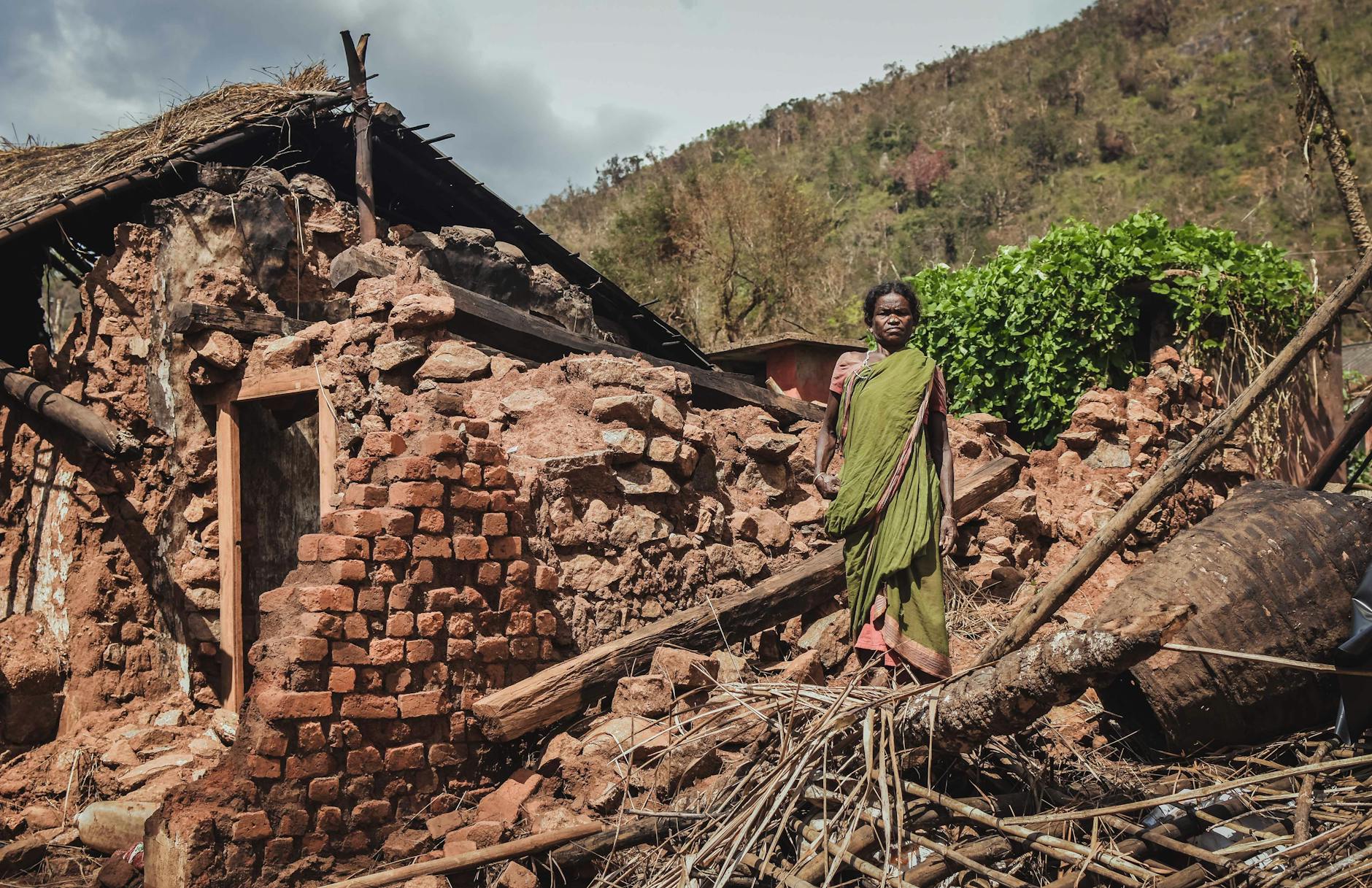 Woman stands in front of a destroyed house after a disaster in rural India, depicting struggle. - rebuild trust infidelity