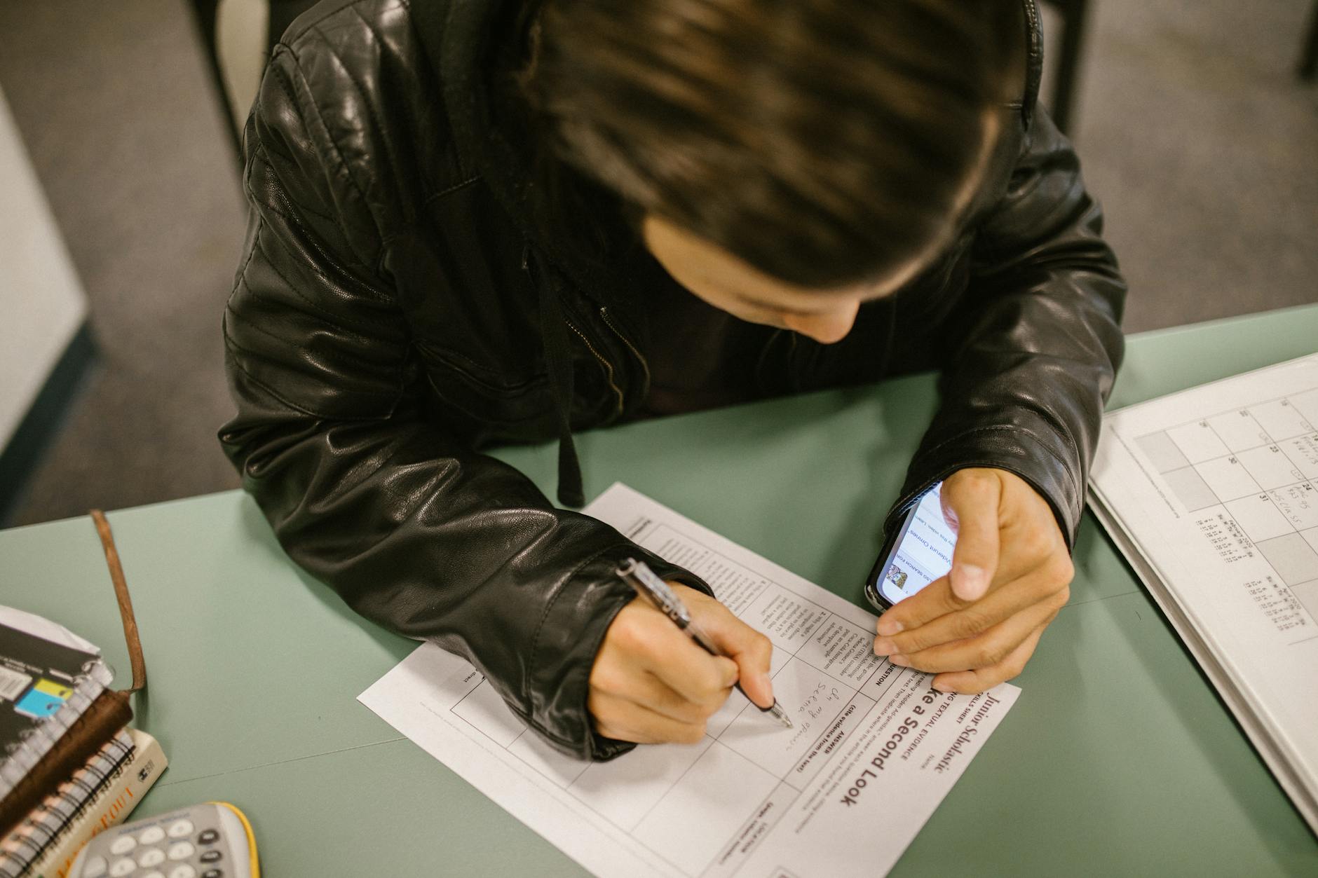An overhead shot of a student using a smartphone to cheat during an exam in a classroom setting. - rebuilding trust cheating