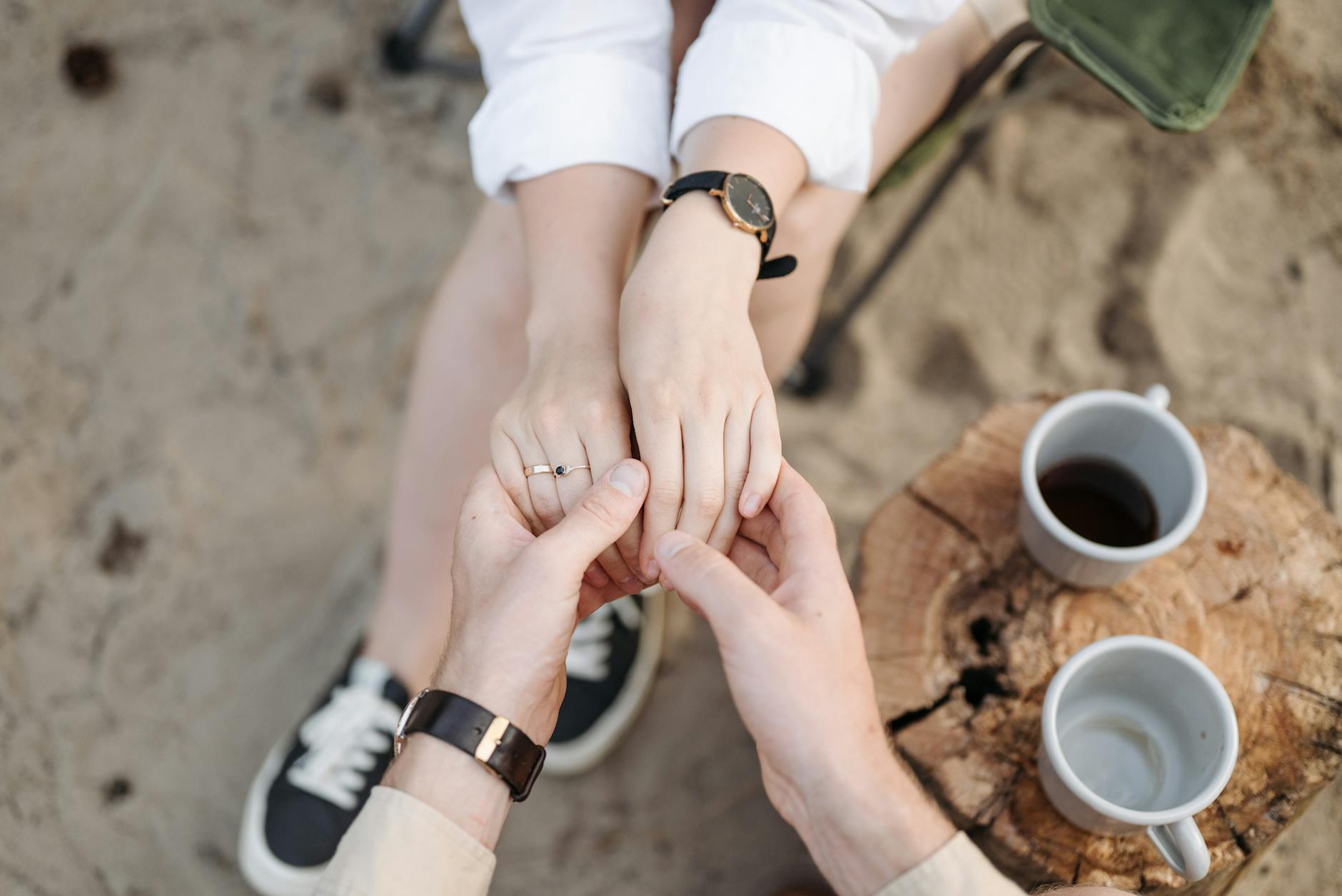 A couple's hands held gently, symbolizing love and connection. Outdoors with coffee cups and a rustic setting. - reconnecting with partner