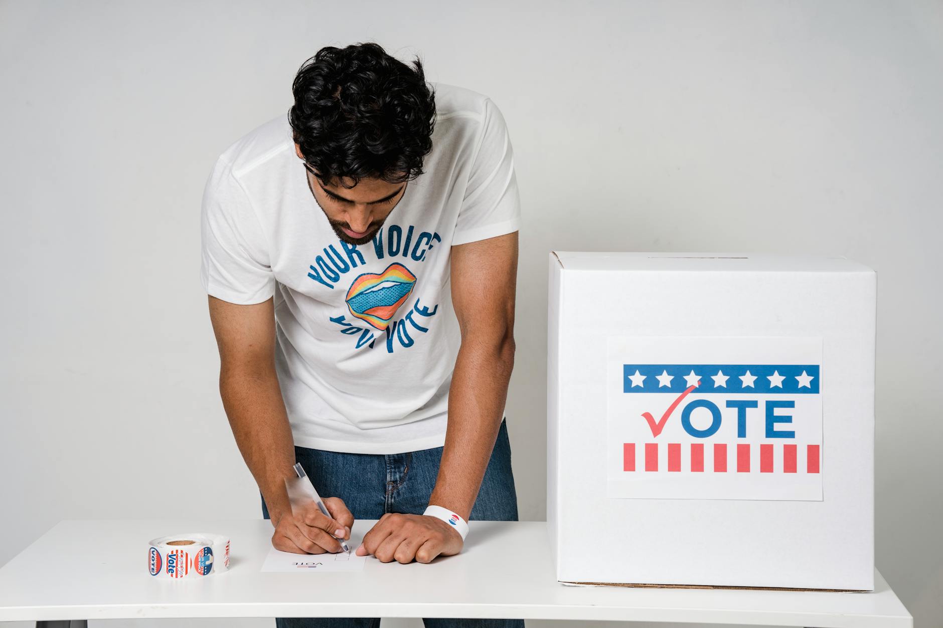 A man writes on a paper to cast his vote next to a ballot box in a studio setting. - refresh your relationship