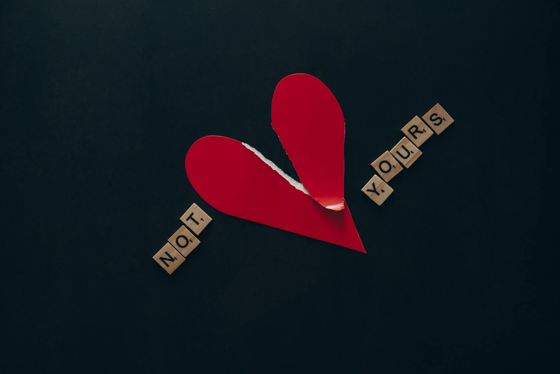 Conceptual image of a torn red heart with Scrabble tiles spelling 'NOT YOURS' on a dark background. - refresh your relationship