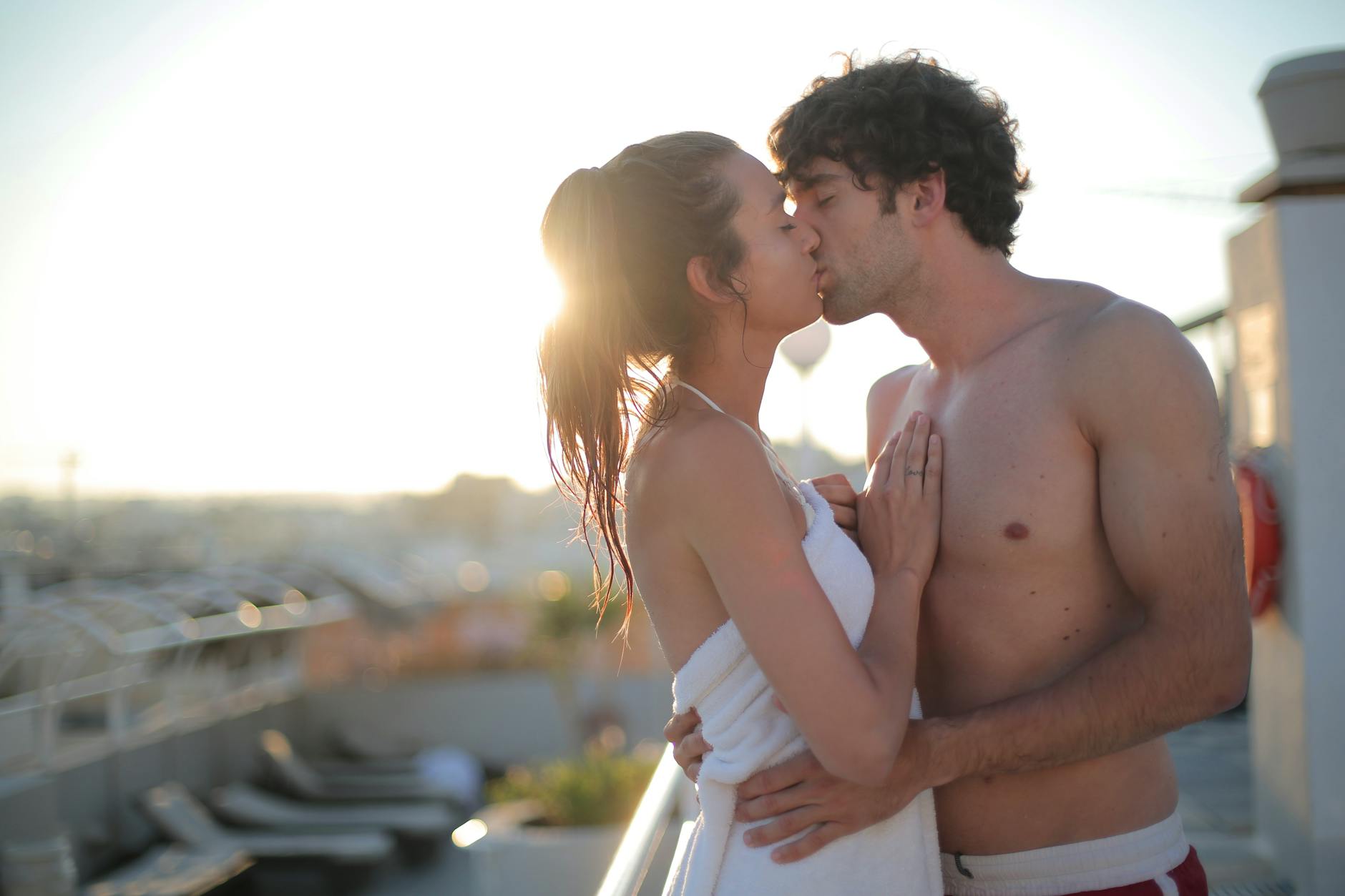 Young couple sharing a kiss on a sunlit balcony, capturing a romantic and intimate moment. - reignite passion relationship