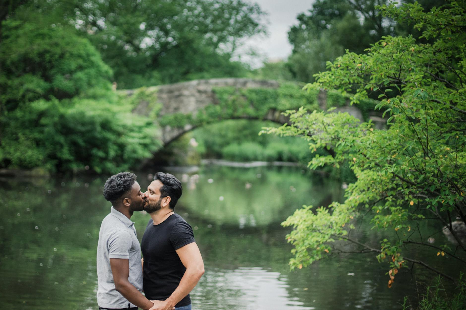 Romantic moment of an interracial gay couple kissing by a scenic park bridge. - rekindle intimacy couples
