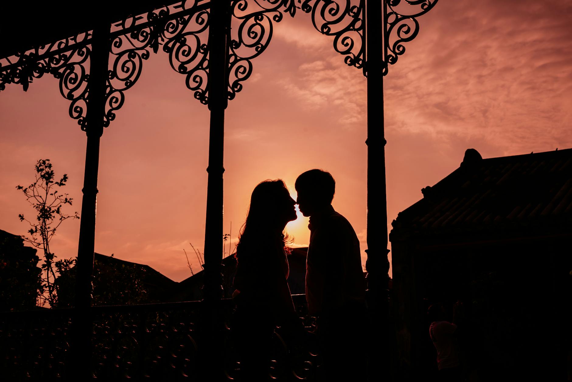 Silhouette of a couple sharing an intimate moment at sunset with ornate ironwork in the foreground. - rekindle romance