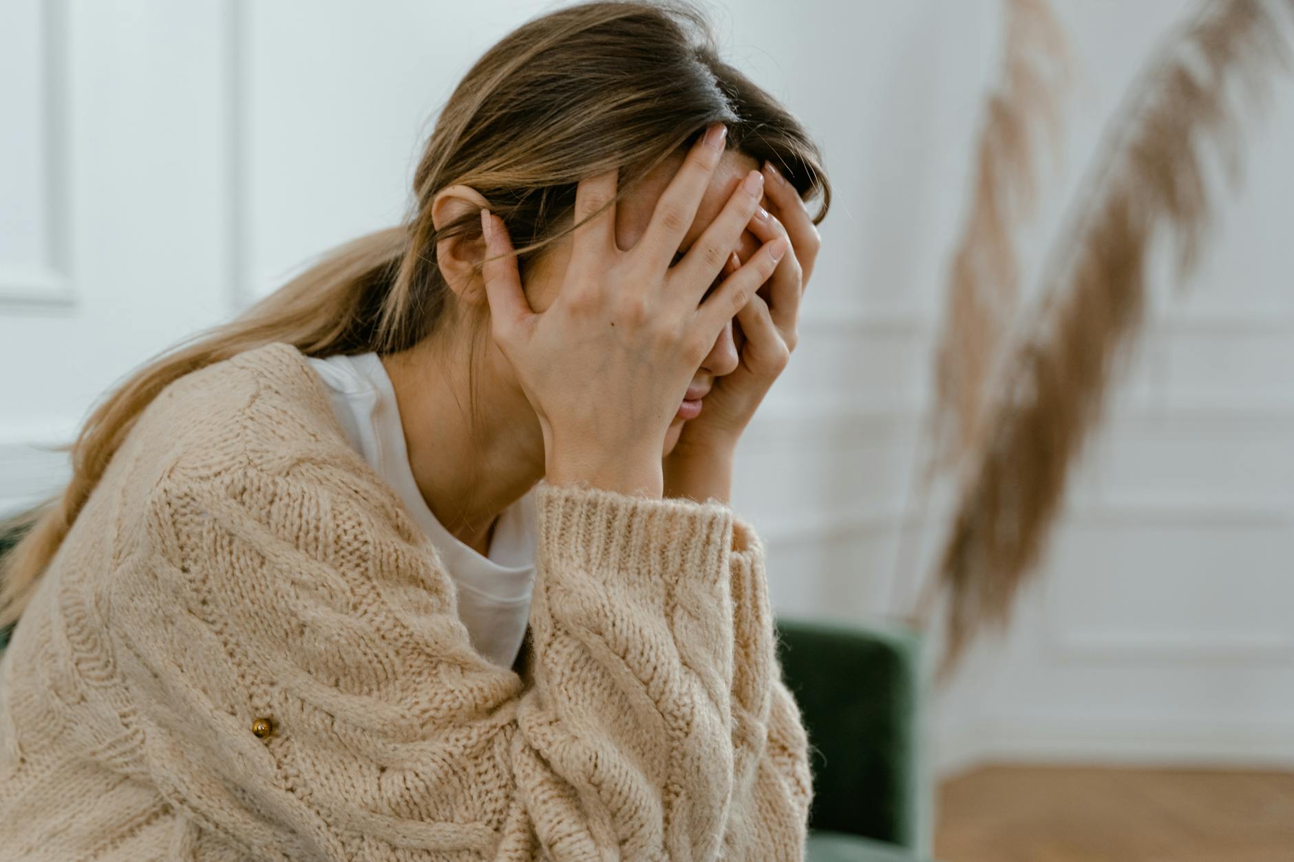 A woman sitting indoors covering her face in frustration, depicting stress and mental health challenges. - relationship anxiety ocd