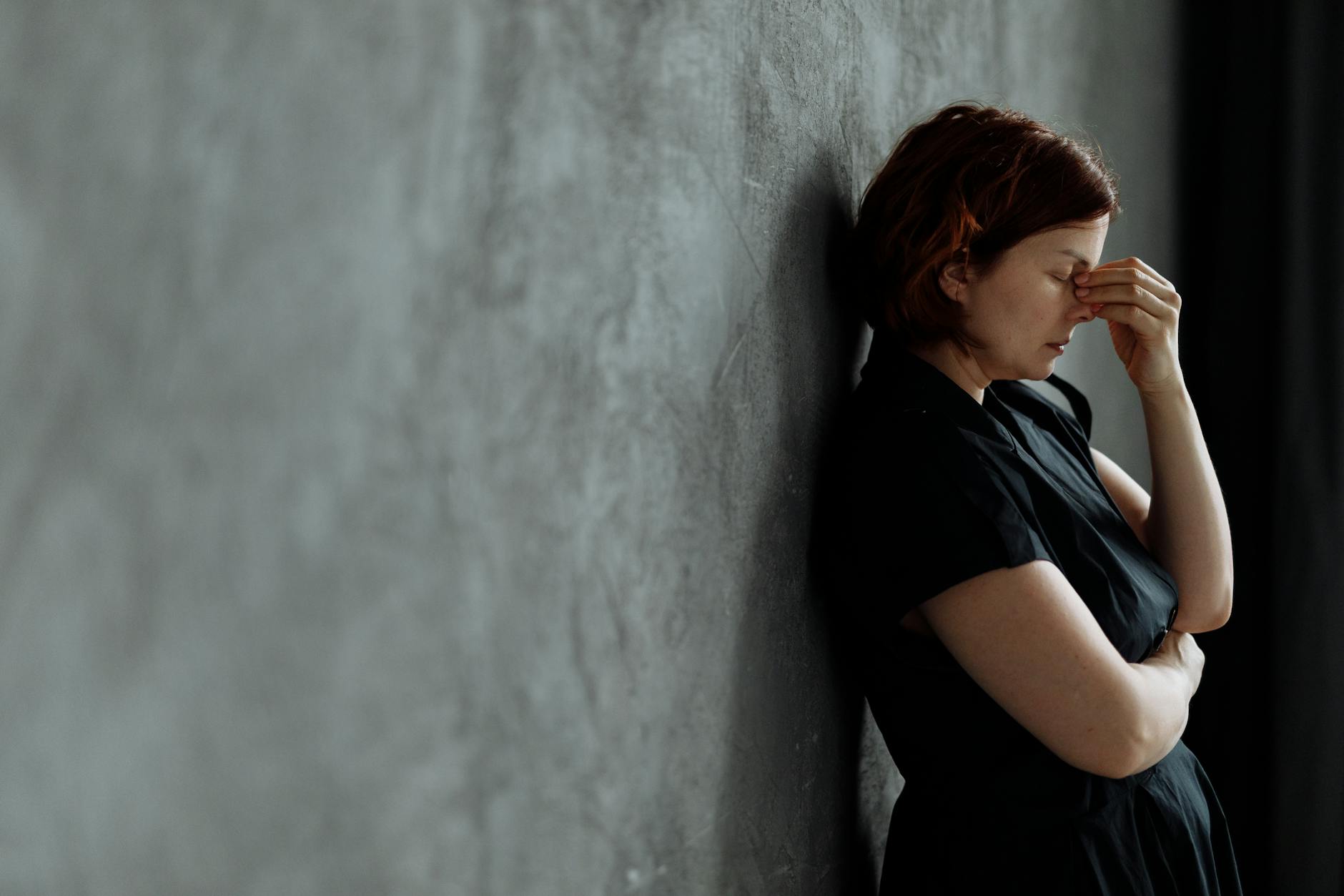 A woman in stress with eyes closed, leaning against a concrete wall indoors. - relationship anxiety ocd