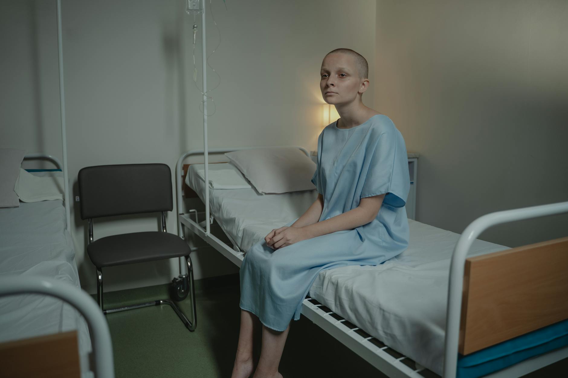 A young woman in a hospital gown sits on a bed in a medical setting, conveying a somber mood. - sad cbt treatment