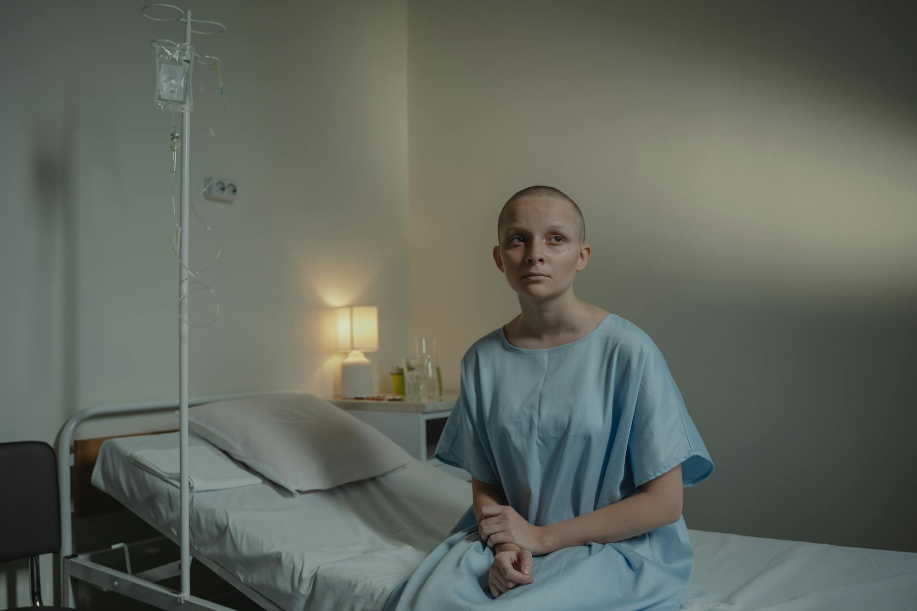 A thoughtful woman in a hospital gown sits on a bed, conveying calmness and reflection. - sad spring treatment