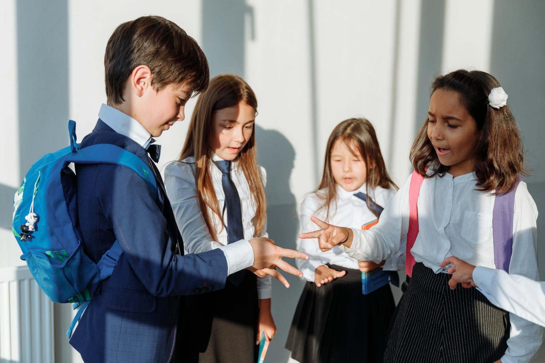 Group of diverse school children in uniform playing rock paper scissors indoors. - school closure activities