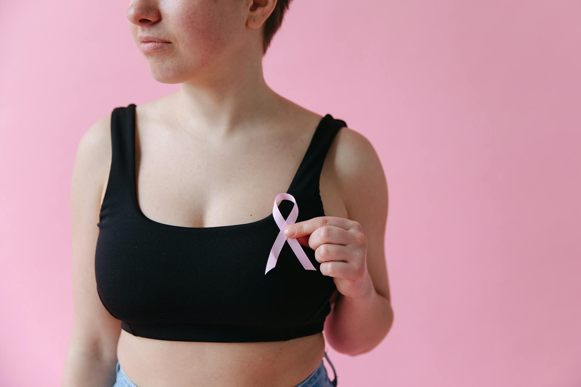 Close-up of a woman holding a pink ribbon symbolizing breast cancer awareness. - self-compassion after failed resolutions
