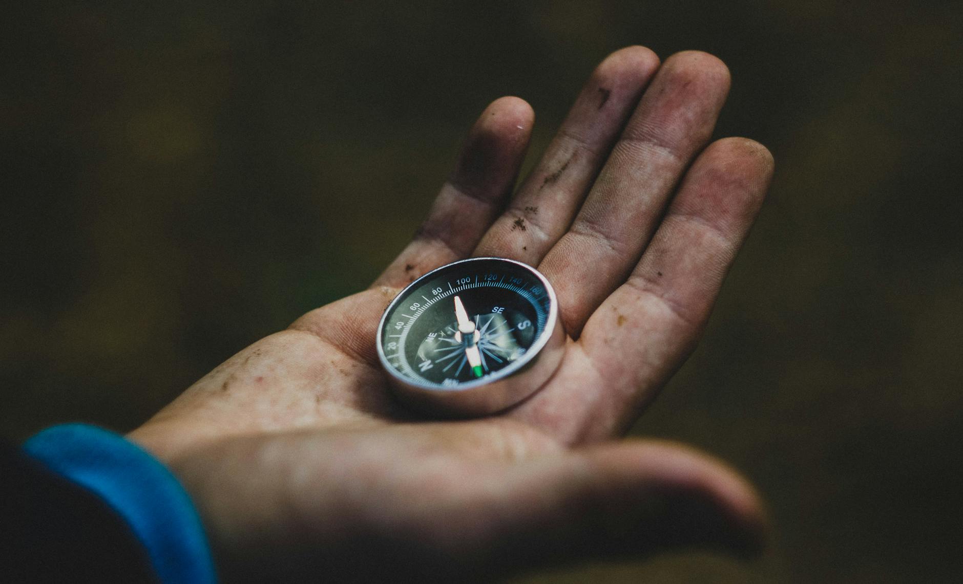 A close-up of a compass held in a dirty hand, symbolizing adventure and navigation. - self compassion outdoors