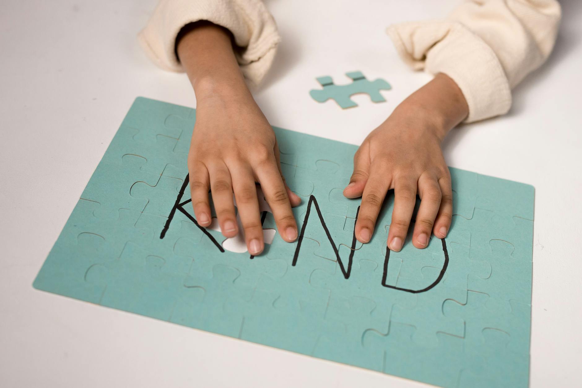 Close-up of child assembling puzzle spelling 'Kind' emphasizing kindness. - self compassion practices
