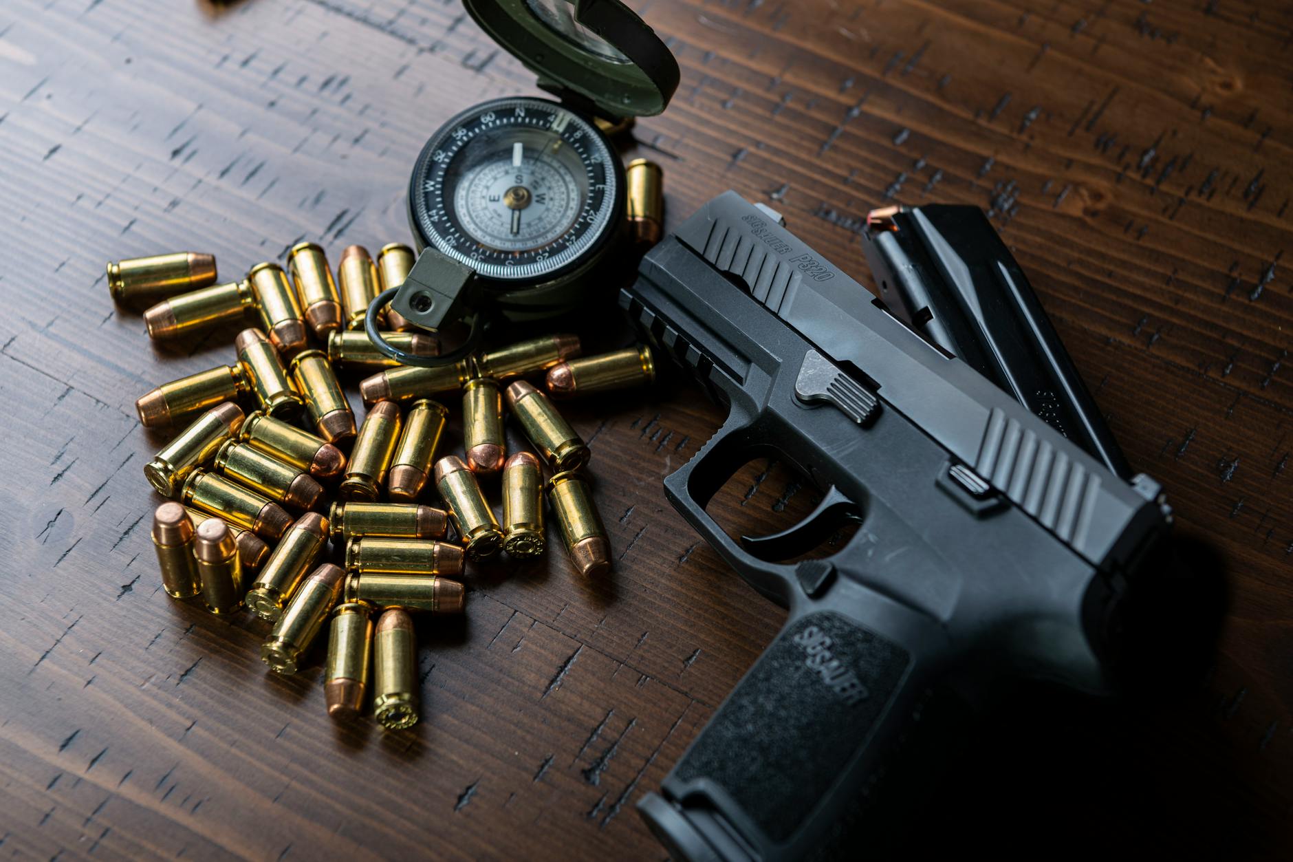 High-angle shot of a handgun, bullets, and a compass resting on a wooden surface. - self-compassion practices