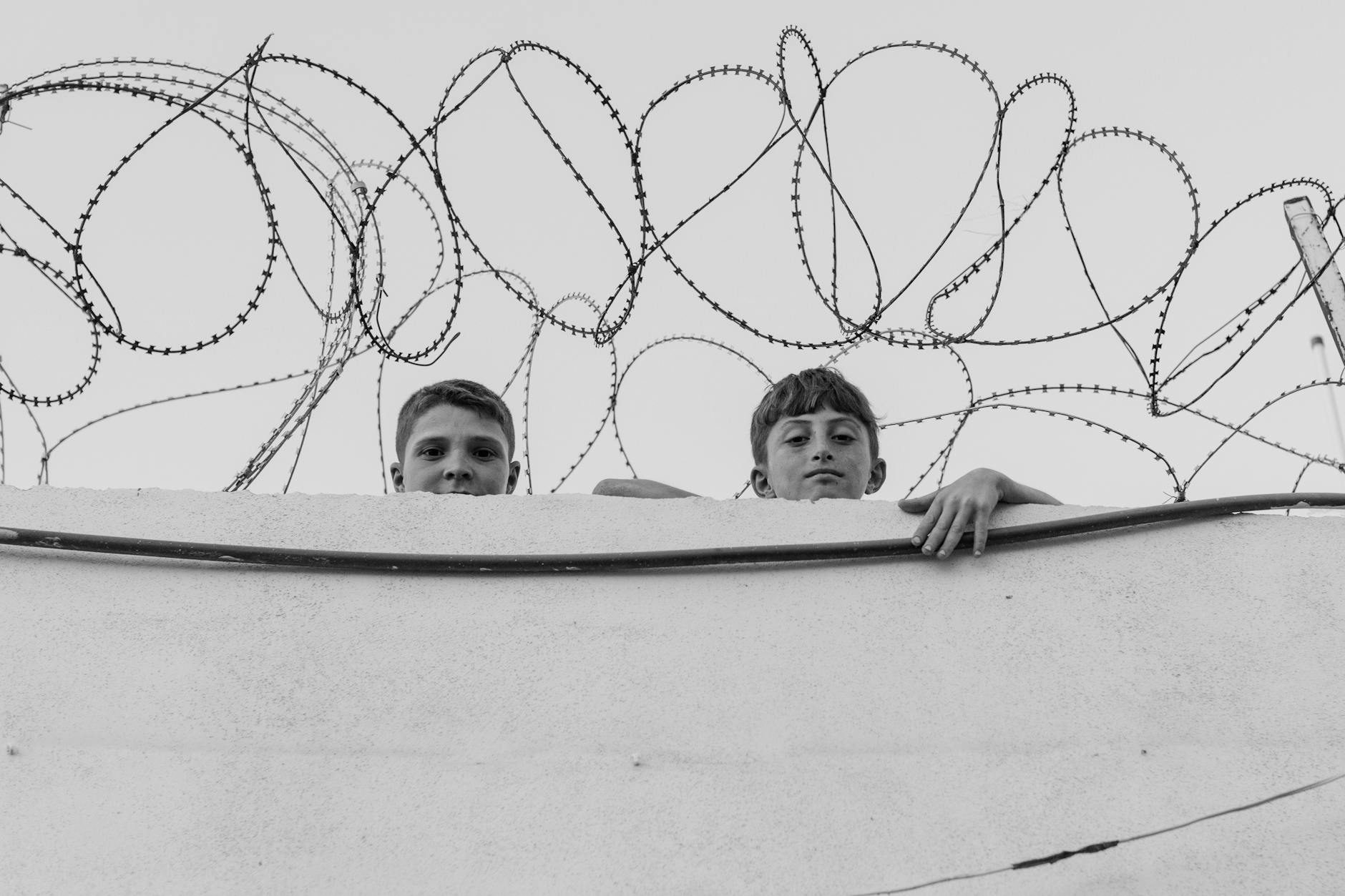 Black and white photo of two boys behind a barbed wire fence in Syria. - setting boundaries adult children