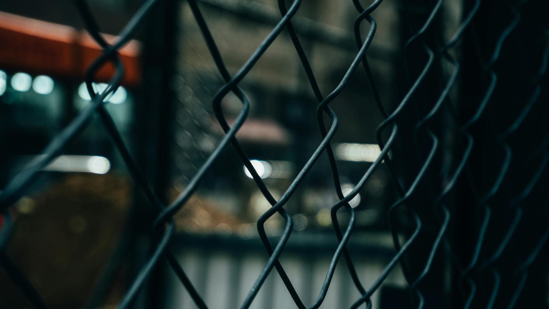 Close-up of a chain link fence with bokeh lights in the background, creating a moody atmosphere. - setting boundaries after isolation
