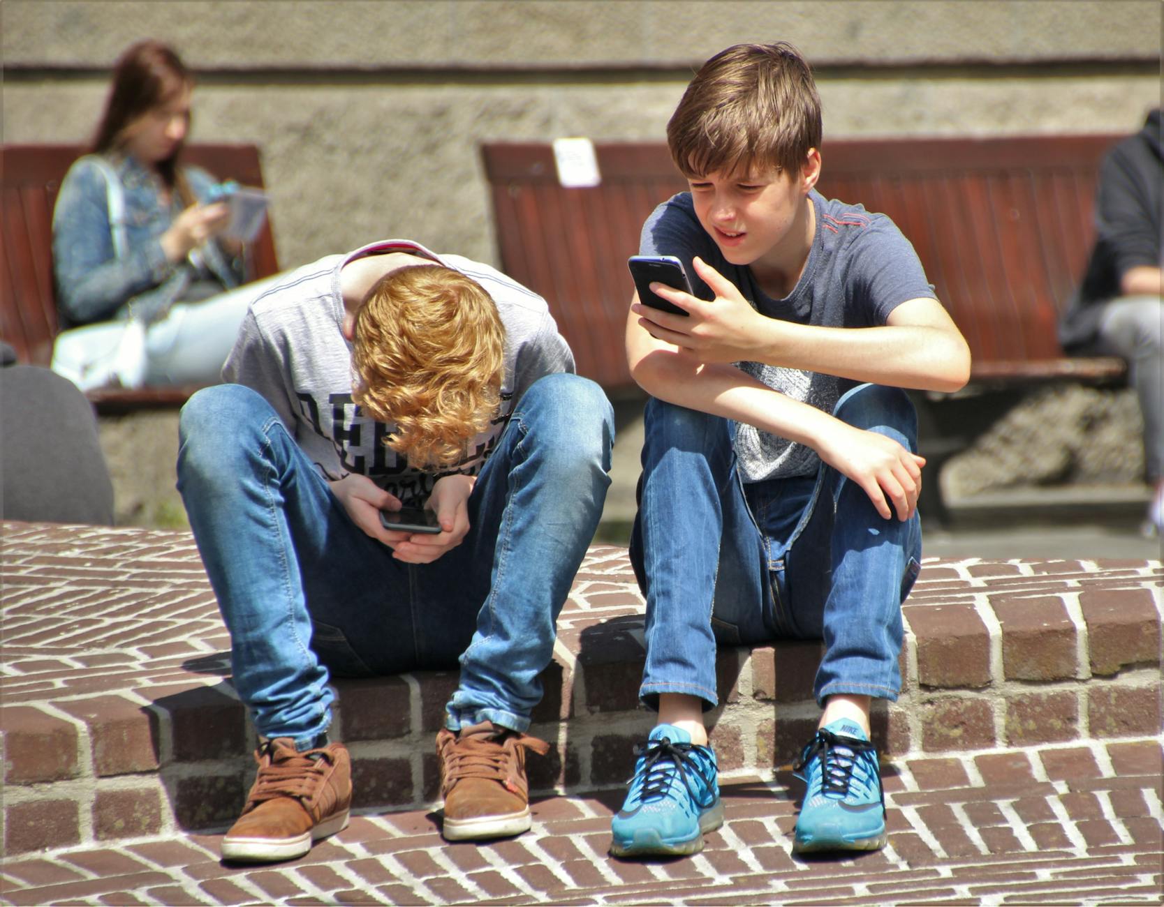 Two teenagers seated outdoors, focused on their smartphones, embracing modern technology. - social media effects on teens