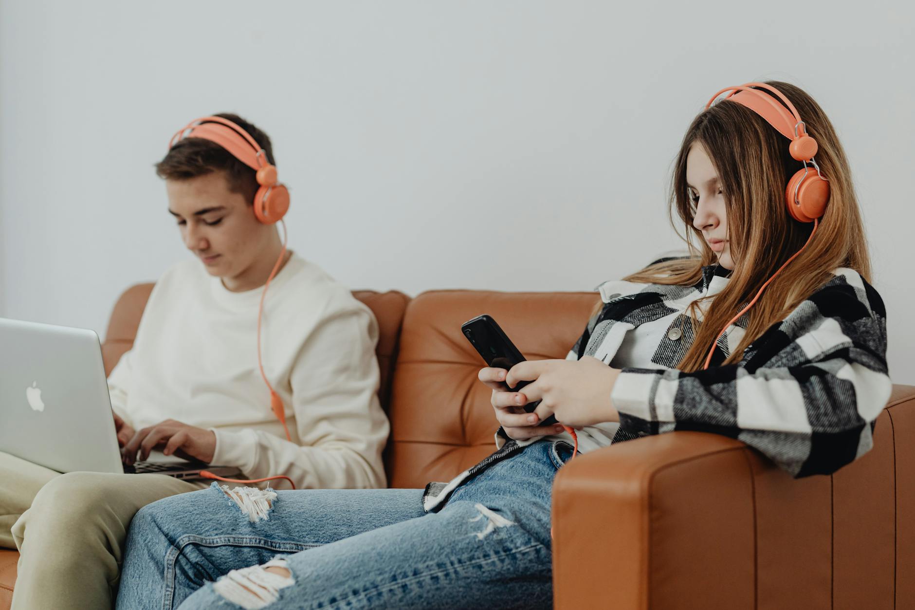 Two teenagers using electronics with headphones on a couch, showcasing modern technology engagement. - social media effects on teens