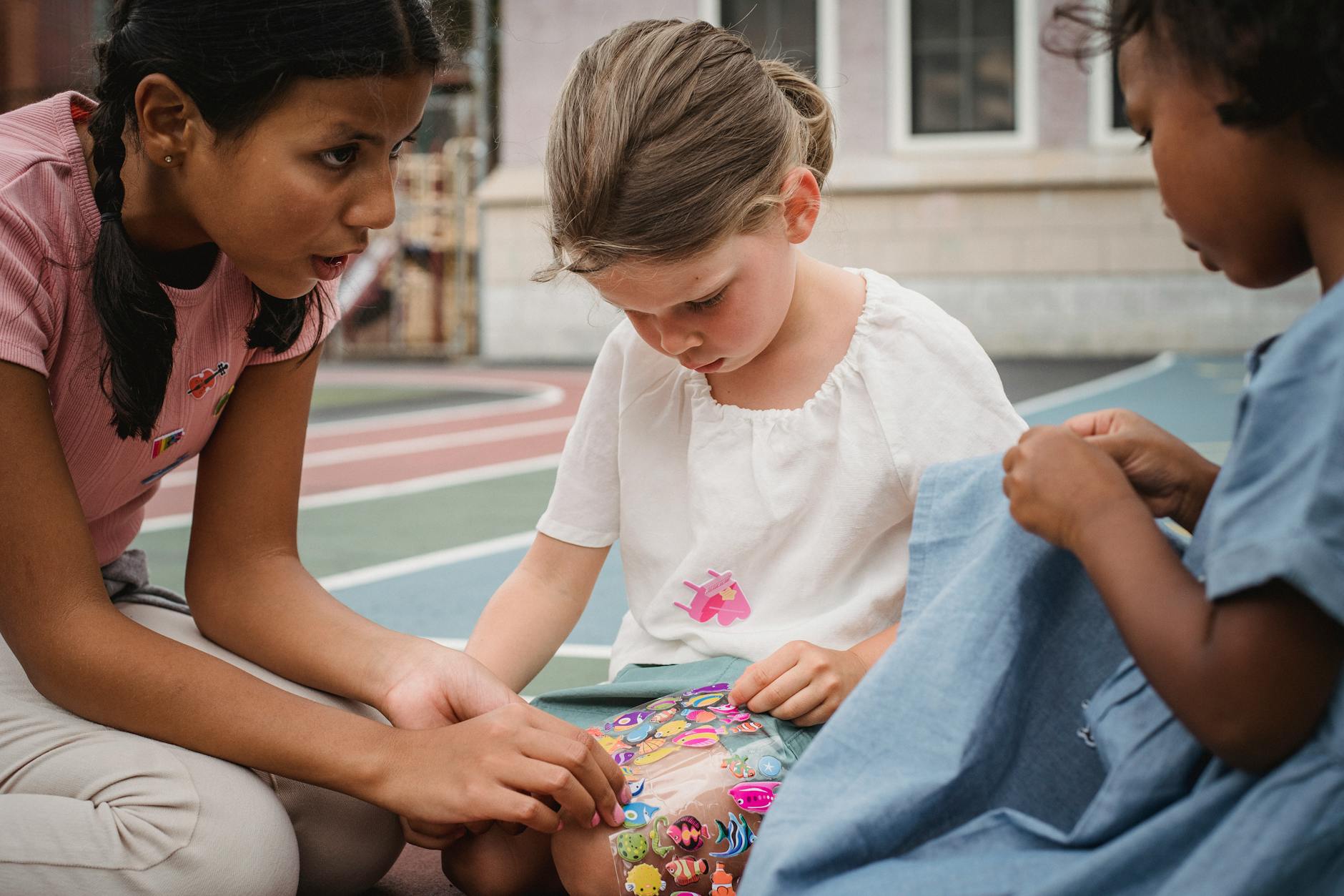Three diverse children playing with stickers on an outdoor playground. - social skills activities