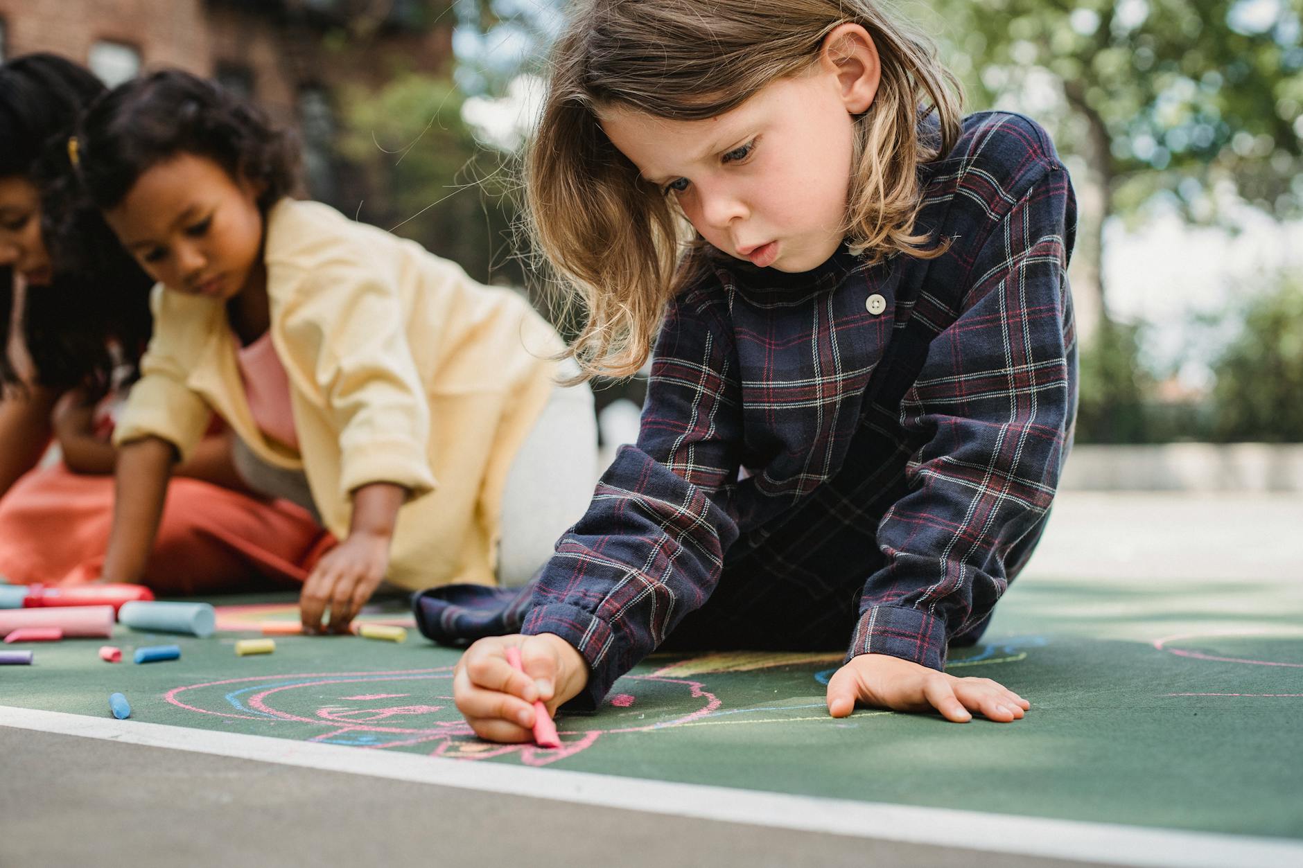 Kids engaged in creative chalk drawings on an outdoor playground with vibrant colors. - social skills activities