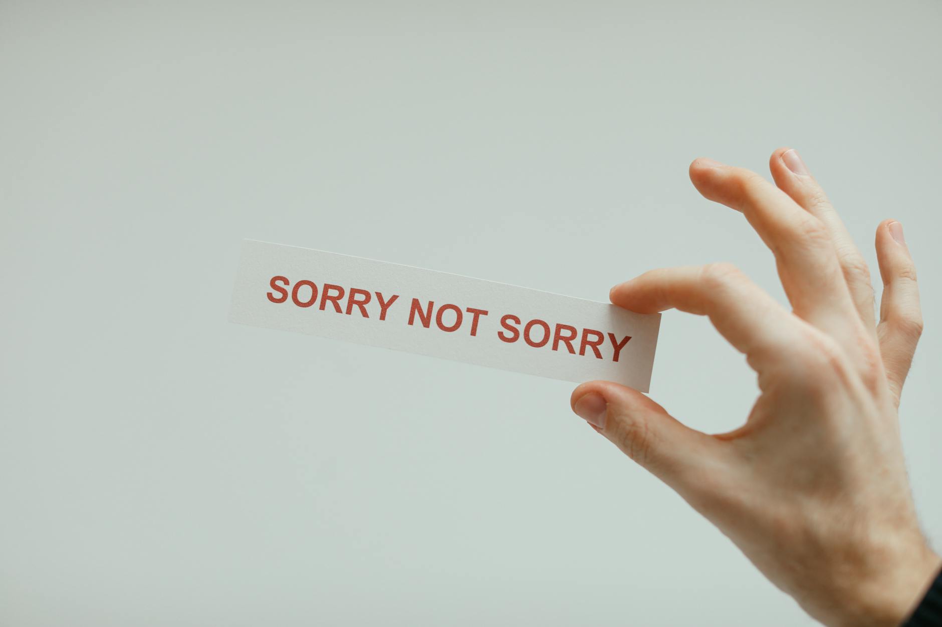 Hand holding a card with the phrase 'Sorry Not Sorry' on a neutral background. - how to spell apologize