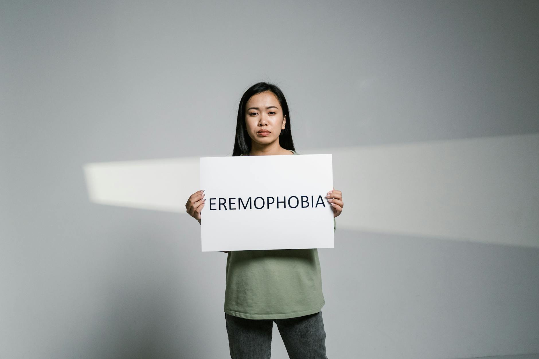 A woman in a studio holds a sign reading 'Eremophobia,' illustrating solitude and anxiety. - spring anxiety adults
