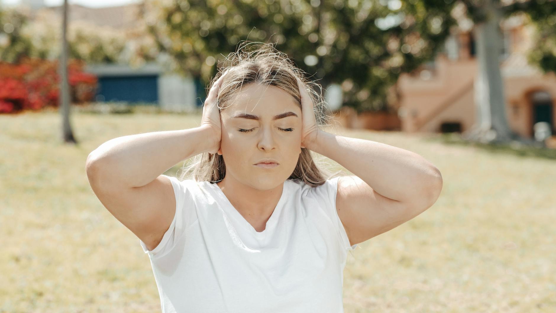 Caucasian woman in a park, eyes closed, holding head in pain hinting at a headache or migraine. - spring anxiety adults